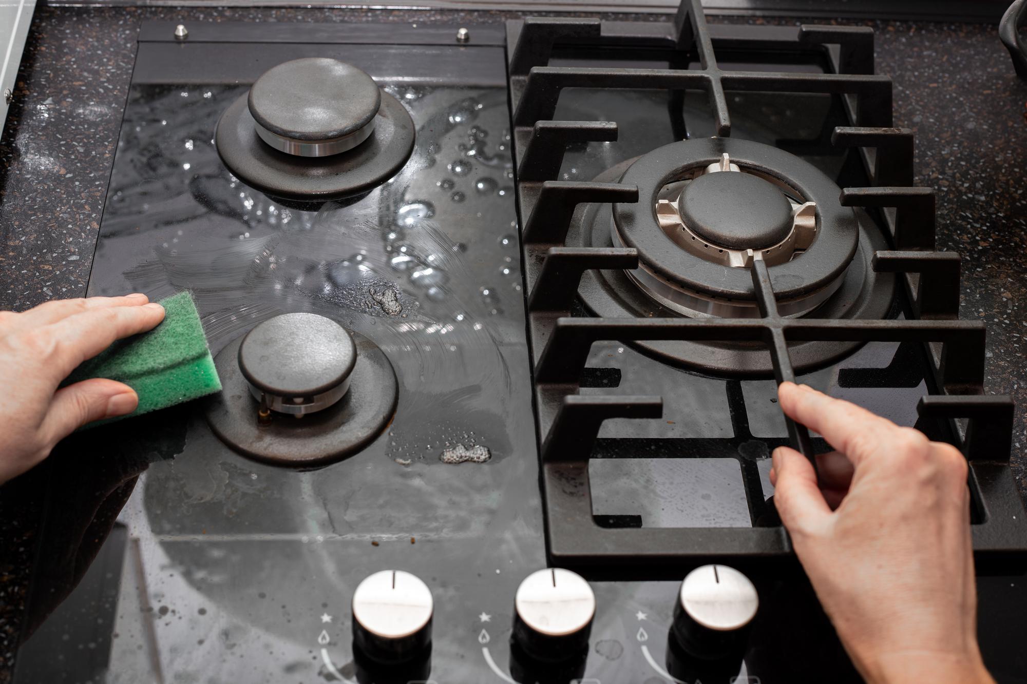 Uma de casa limpa o fogão a gás da cozinha com uma esponja Manutenção de vidro temperado e vitrocerâmica