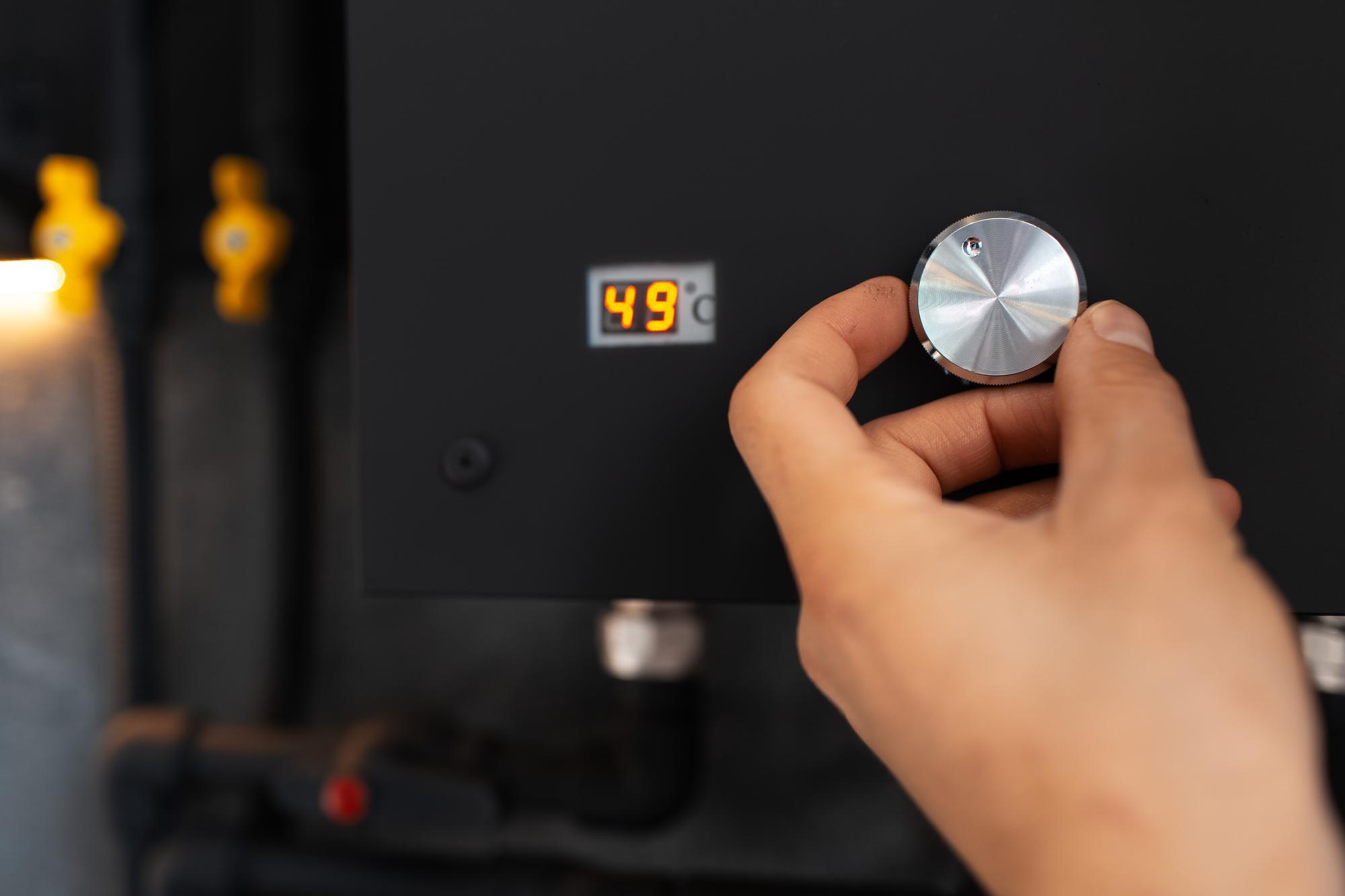 Mão masculina que ajusta a temperatura no aquecedor a gás de água de cor preta