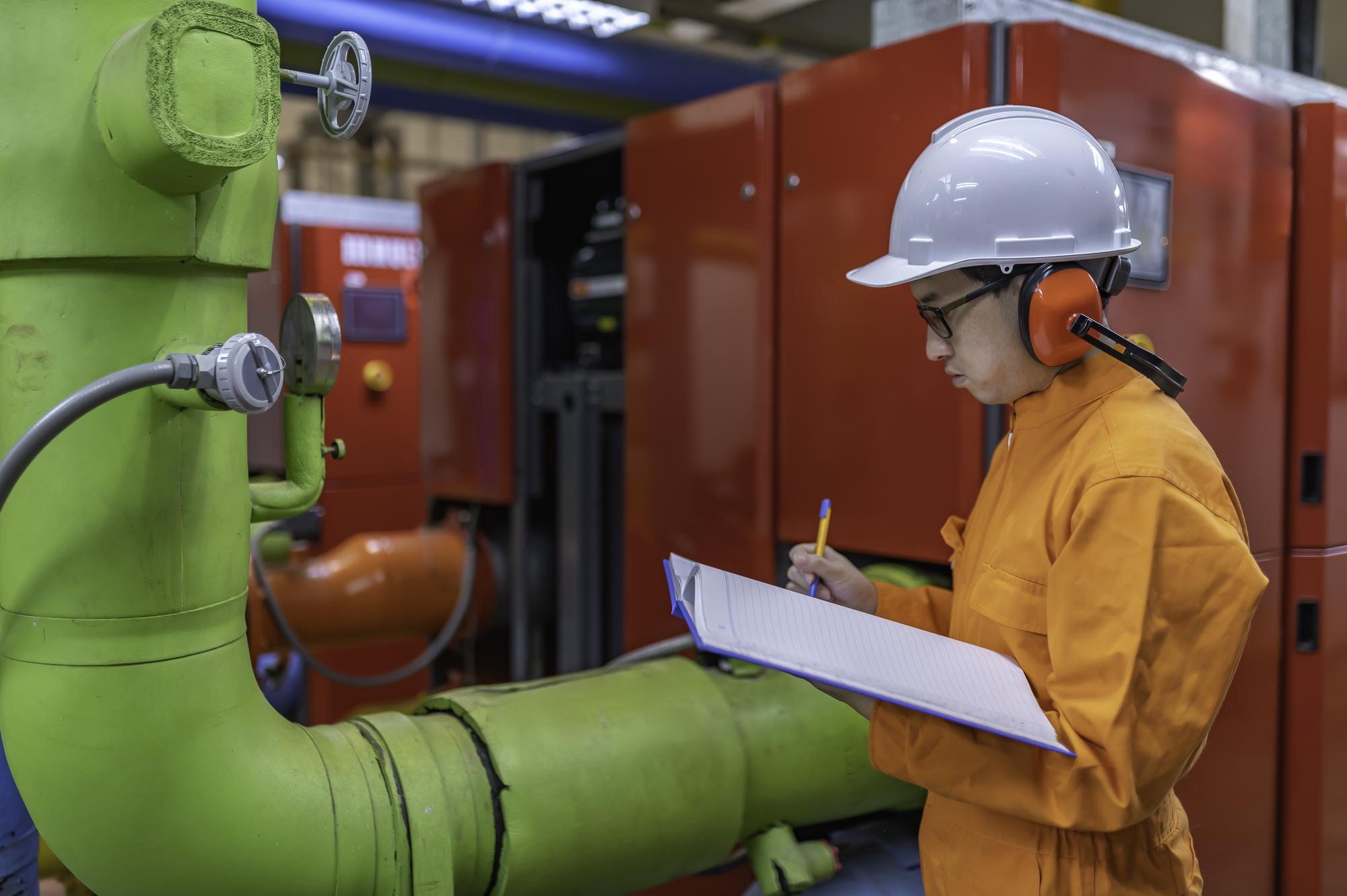 Técnico de manutenção em usina de aquecimentoTrabalhadores petroquímicos supervisionam operação de gasodutos e oleodutos na fábricaEngenheiros colocam protetor auditivo em sala com muitos canos