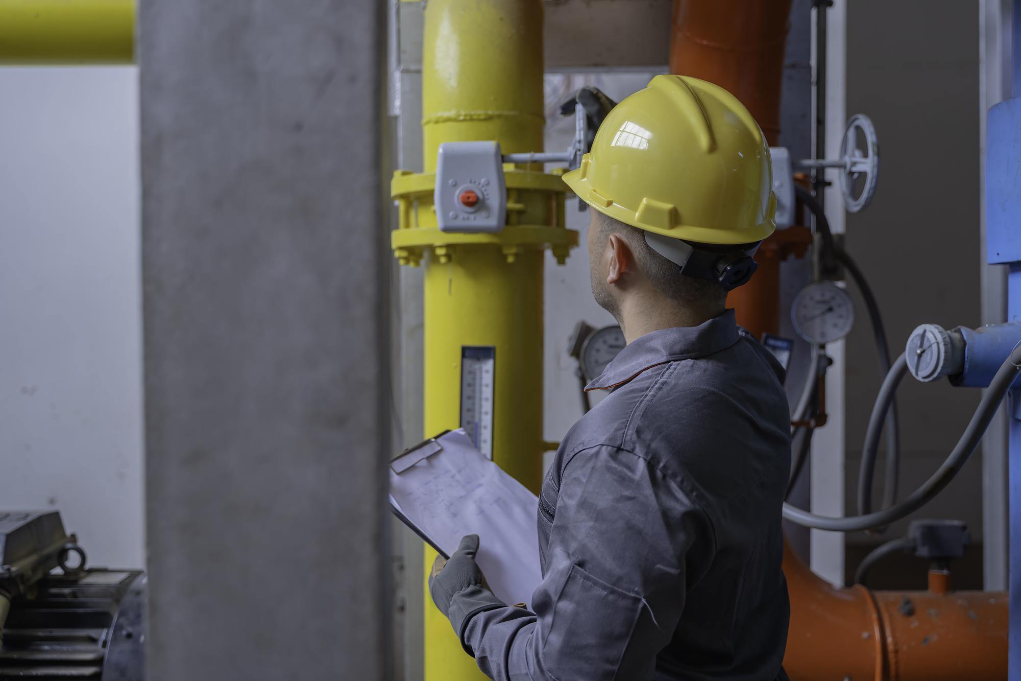 Engenheiro asiático usando óculos trabalhando na manutenção da sala da caldeira verificando dados técnicos do equipamento do sistema de aquecimentoTailândia