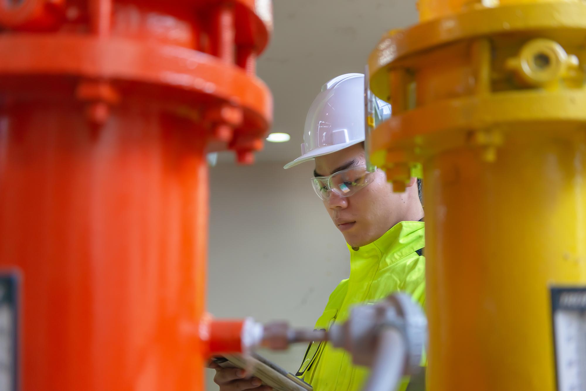 Engenheiro asiático usando óculos trabalhando na manutenção da sala da caldeira verificando dados técnicos do equipamento do sistema de aquecimentoTailândia