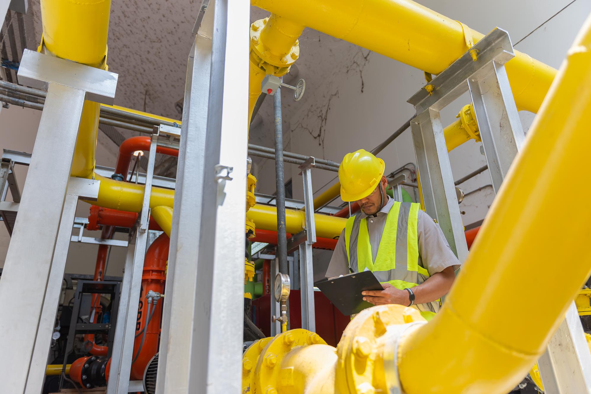Engenheiro asiático usando óculos trabalhando na manutenção da sala da caldeira verificando dados técnicos do equipamento do sistema de aquecimentoTailândia