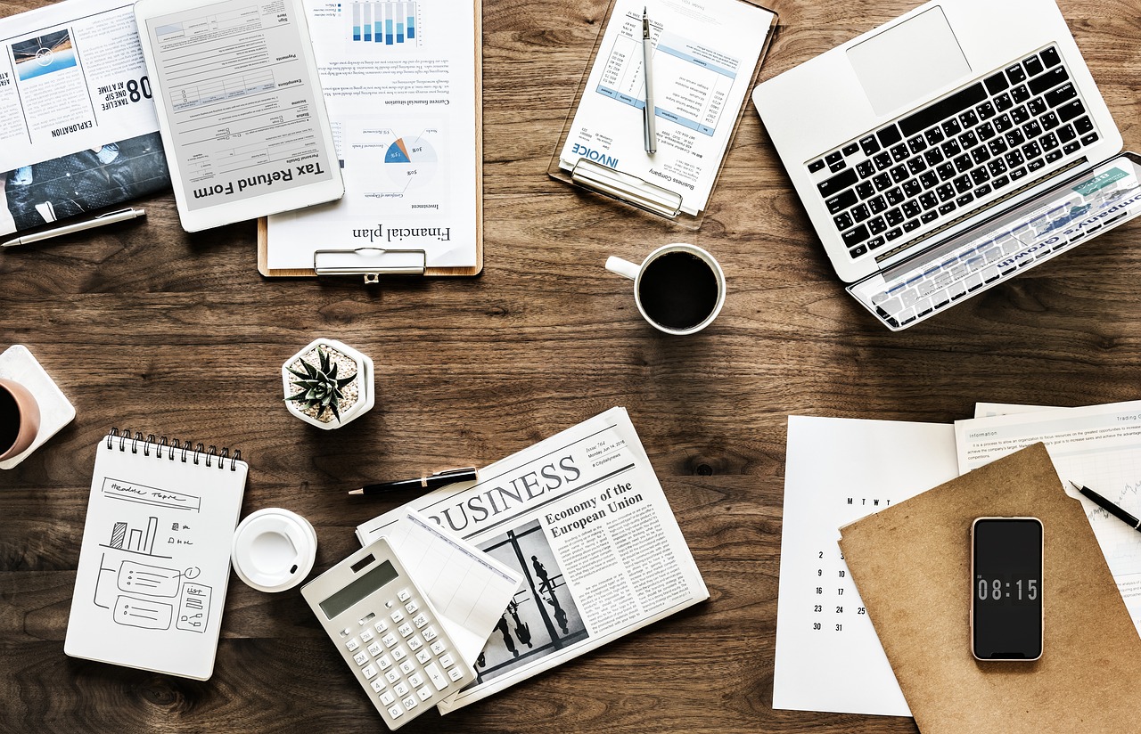Empresário analisando planta de empreendimento imobiliário em mesa de madeira maciça com dispositivos digitais ao redor