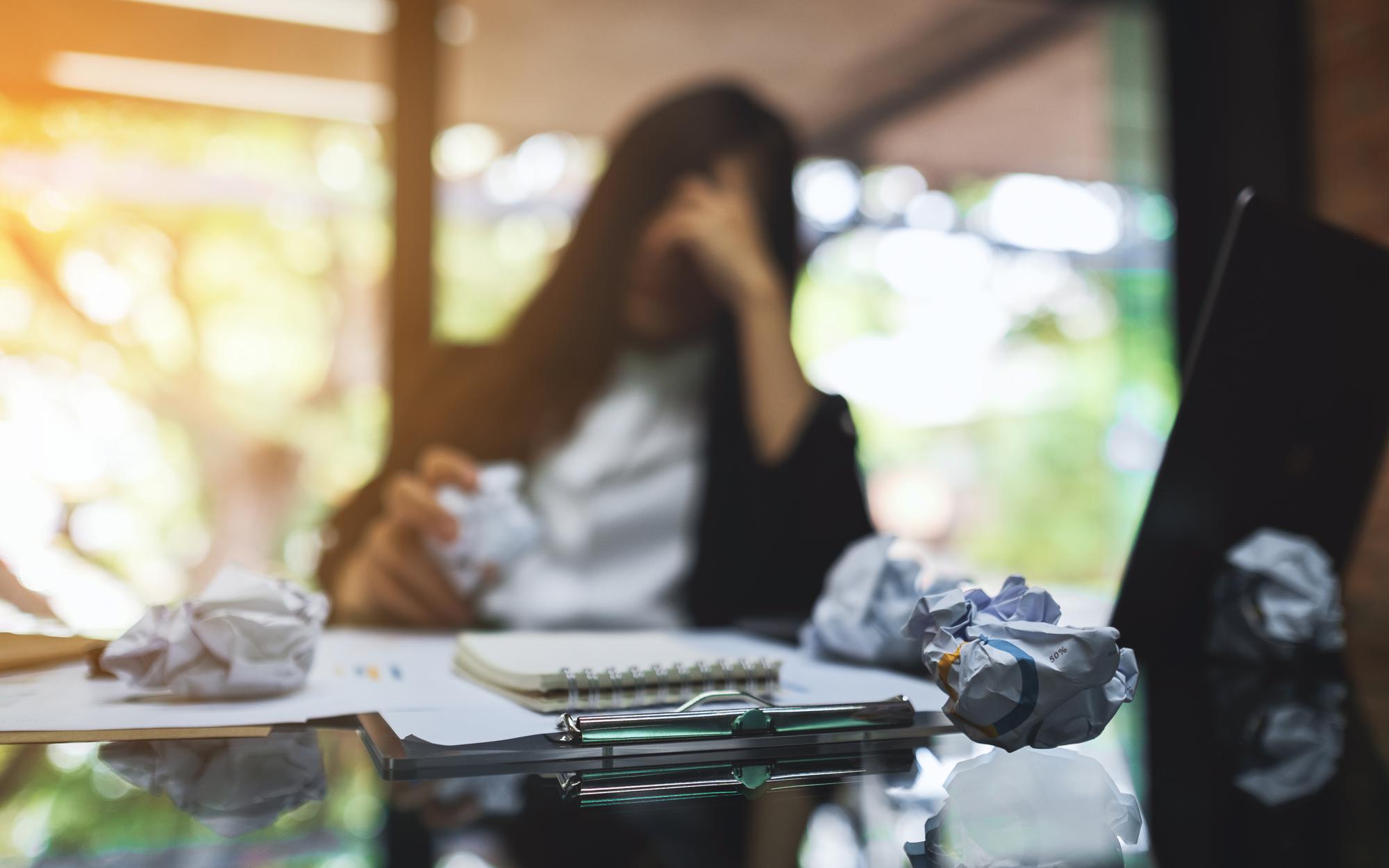 Mulher de negócios fica estressada com papéis e laptop bagunçados na mesa enquanto tem um problema no trabalho no escritório