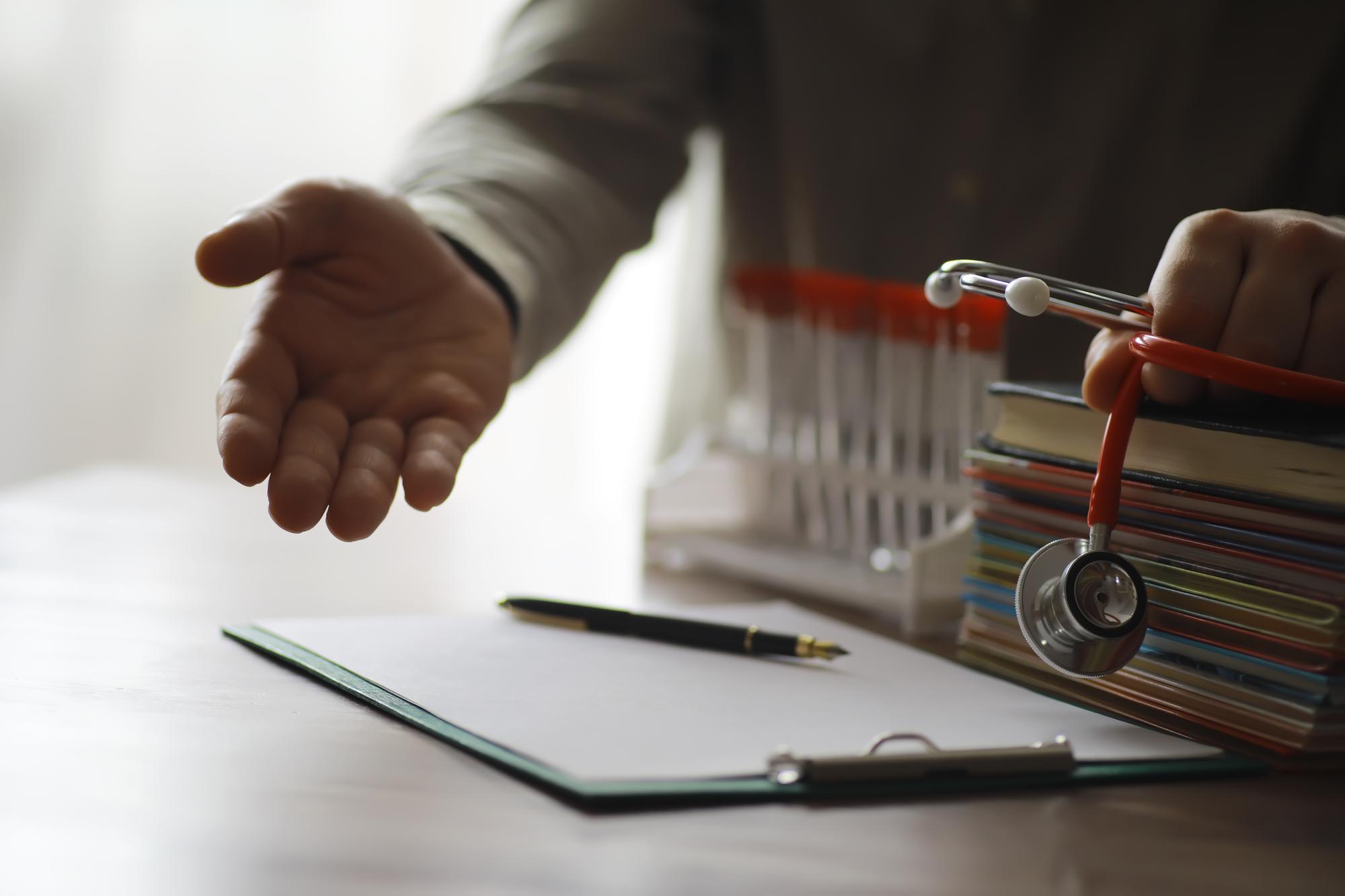 Médico masculino pesquisa informações em livro e estetoscópio médico de prescrição escrita na mesa na clínica Conhecimento médico e conceito de educação