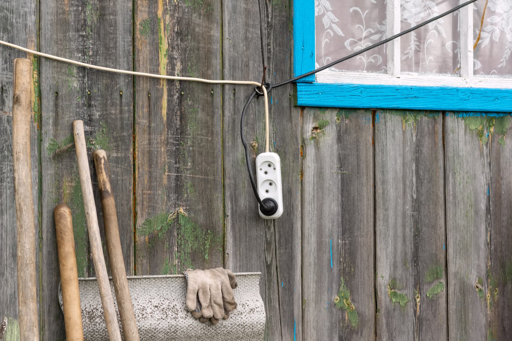 Um fio elétrico com uma tomada está pendurado na parede de madeira da casa perto da janela