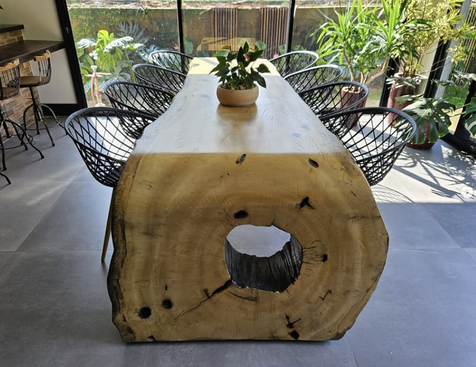 Mesa cascata de madeira maciça com bordas orgânicas integrando uma sala de jantar minimalista com tons de roxo e iluminação natural