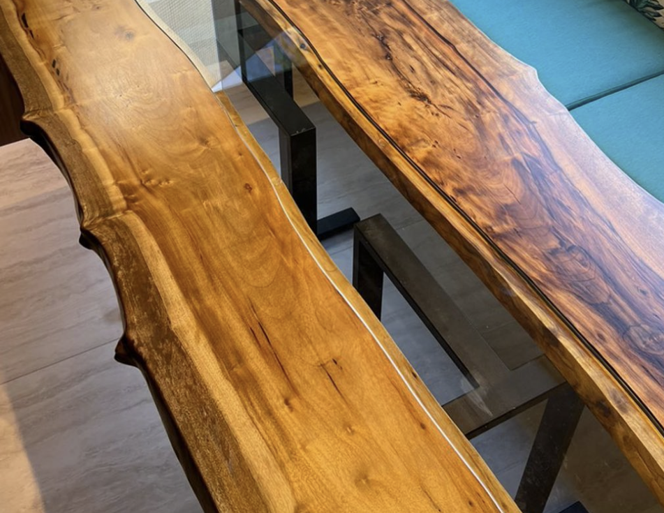Mesa de jantar de madeira maciça com bordas orgânicas em uma sala ampla com iluminação natural e plantas ao fundo