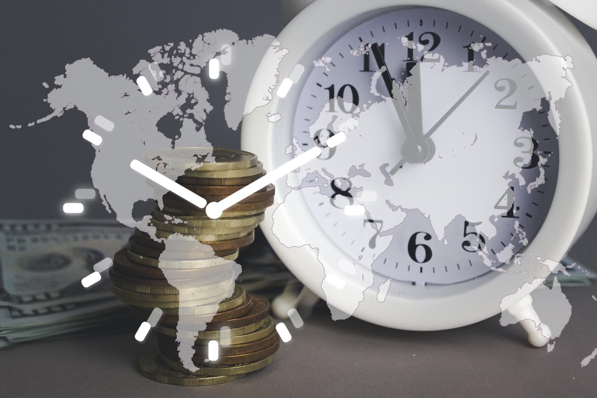 Relógio de alarme branco com pilha de moedas e pilha de notas de cem dólares com o planeta Terra Digital Símbolo do mapa mundial global e símbolo do relógio branco em fundo cinzento Economize dinheiro O tempo é um conceito de dinheiro