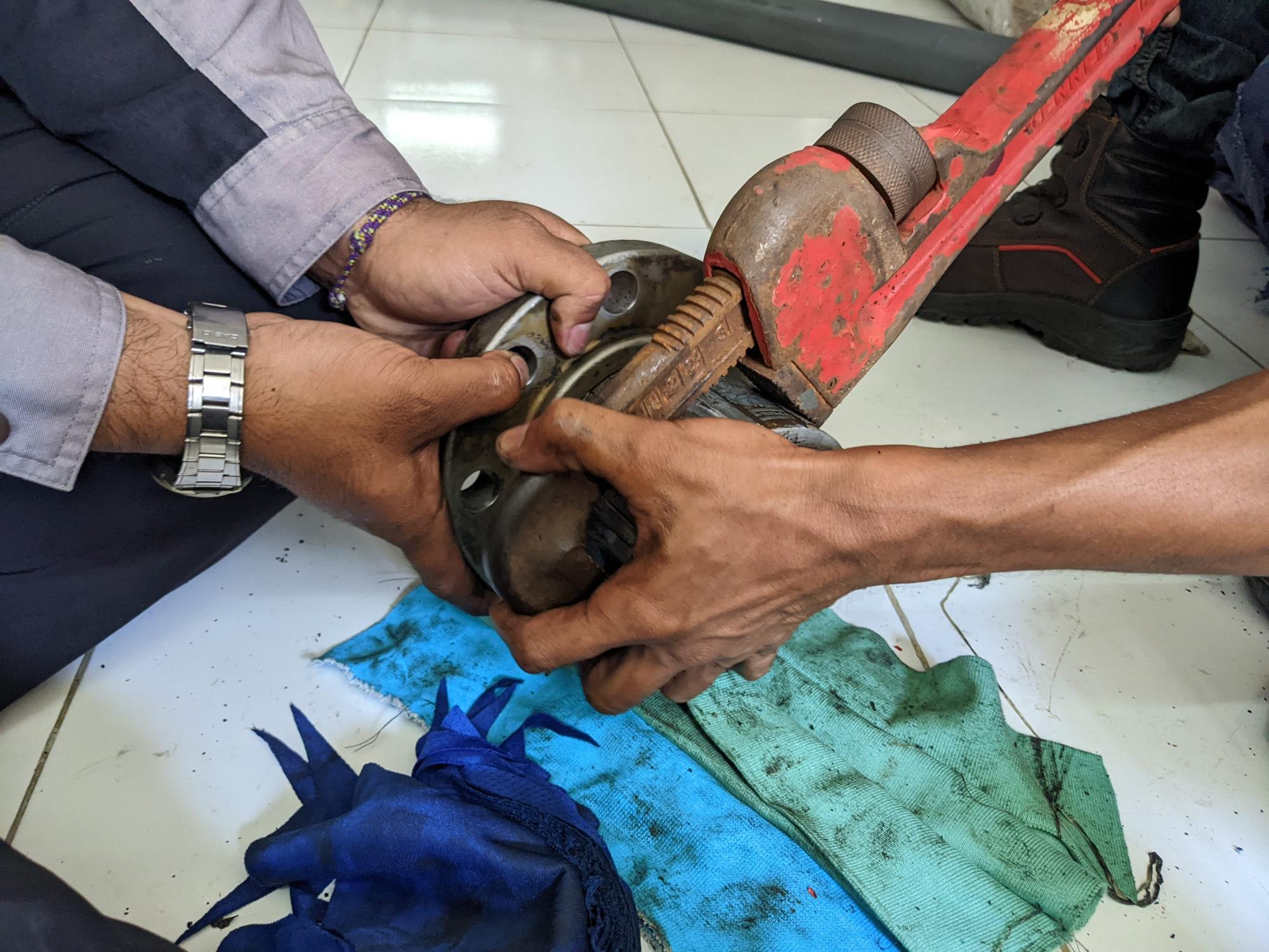 Dois homens trabalhando para remover a junção do tubo com a chave do tubo