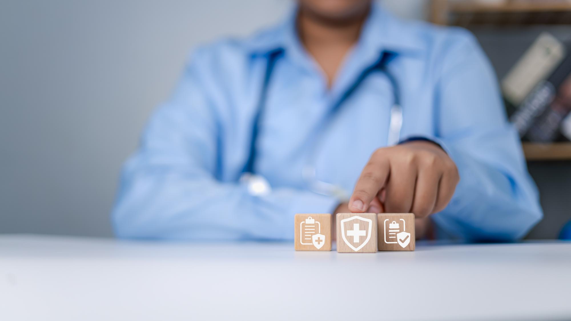 Conceito de seguro de saúde Tratamento de doenças Saúde e acesso ao bem-estar conceito de saúde Médico de mão segurando empilhamento de madeira com cuidados de saúde ícones médicos e hospitalares na mesa Mais sinal no bloco