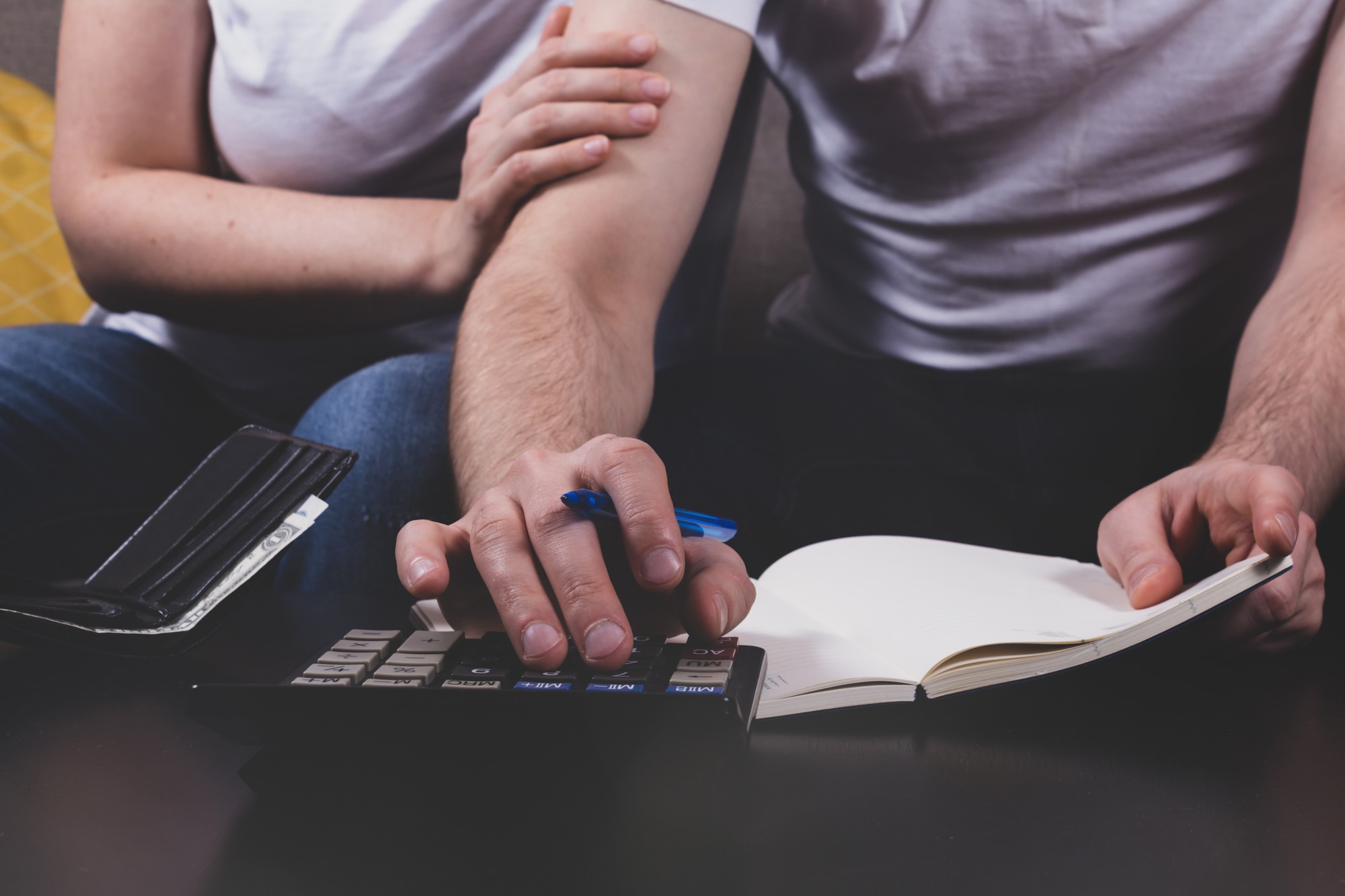 Jovem casal calculando o orçamento familiar sentados juntos no sofá e esposa apoiando o marido em tempos difíceis. Conceito de crise financeira familiar