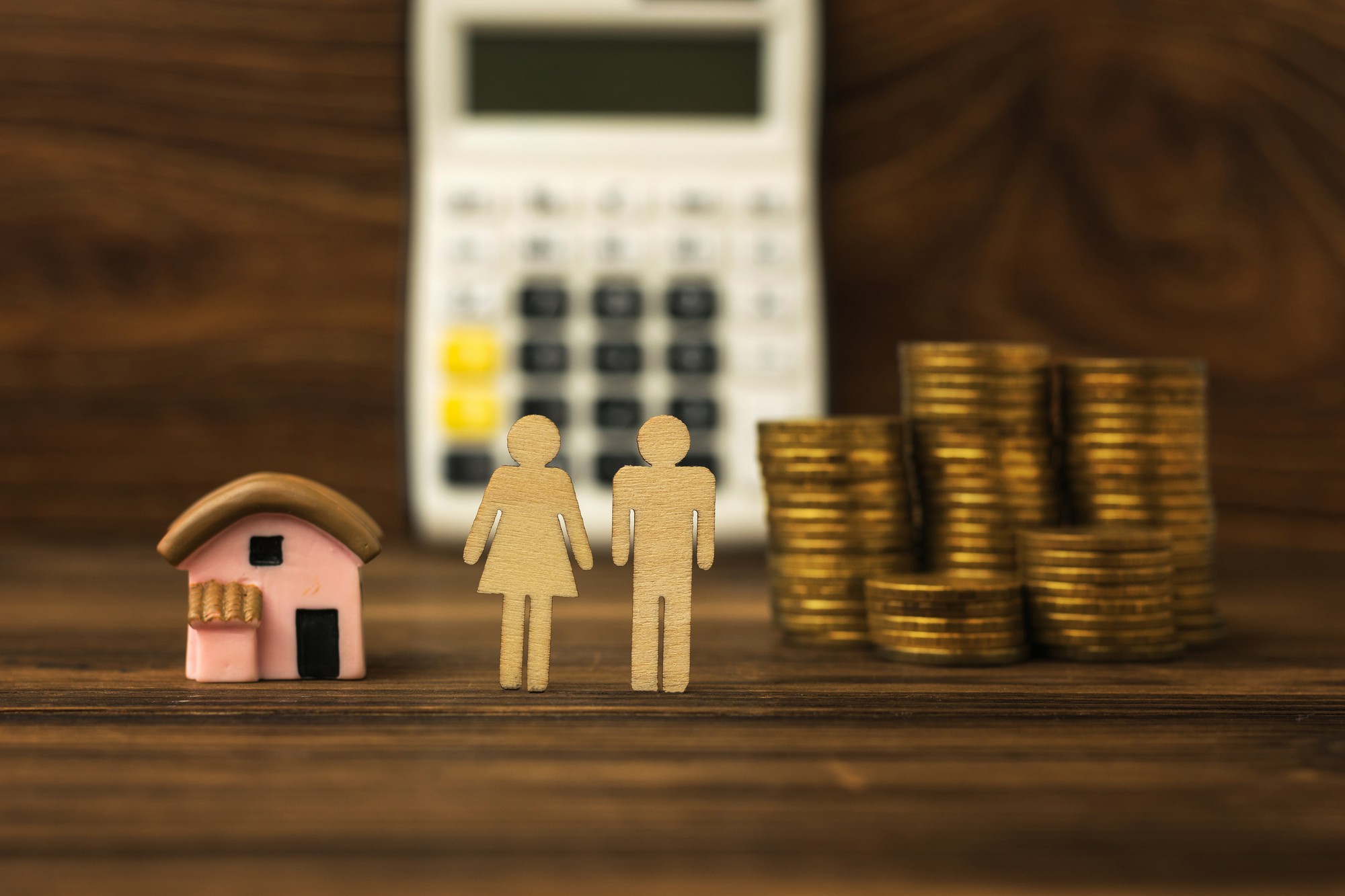 Duas figuras de pessoas, uma casa e moedas no fundo de uma calculadora. O conceito de aquisição de habitação. Hipoteca.