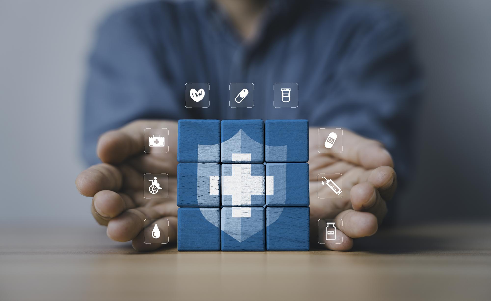 Healthcare insurance and medical protection concept with shield symbol on blue wooden blocks surrounded by caring hands representing health security medical services safety and patient care