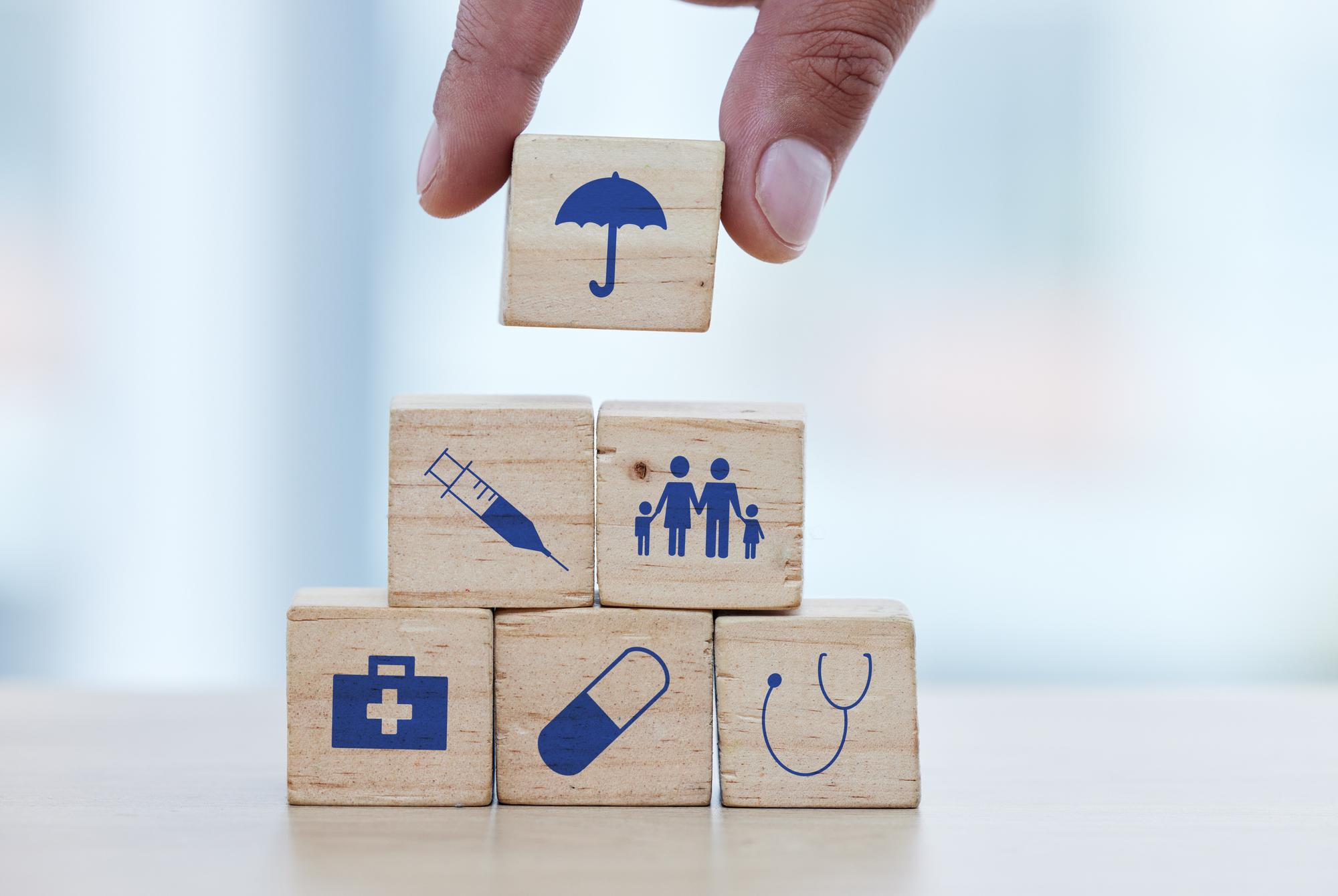 Mãos de madeira e blocos de construção na mesa para seguro de saúde ou uma base segura e saudável Mão do médico colocando pequeno objeto de bloco de madeira ou ícones com guarda-chuva para construir investimento médico