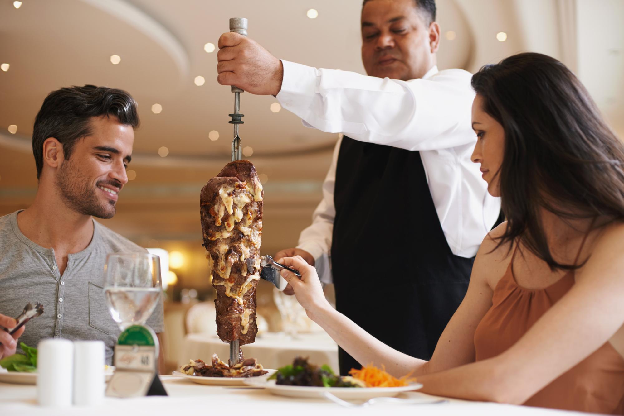 Casal de garçom e serviço para almoço em um restaurante com carne felicidade e refeições requintadas para aniversário ou lua-de-mel homem mulher e empregado com bife em espeto refeição saudável e mesa em Londres