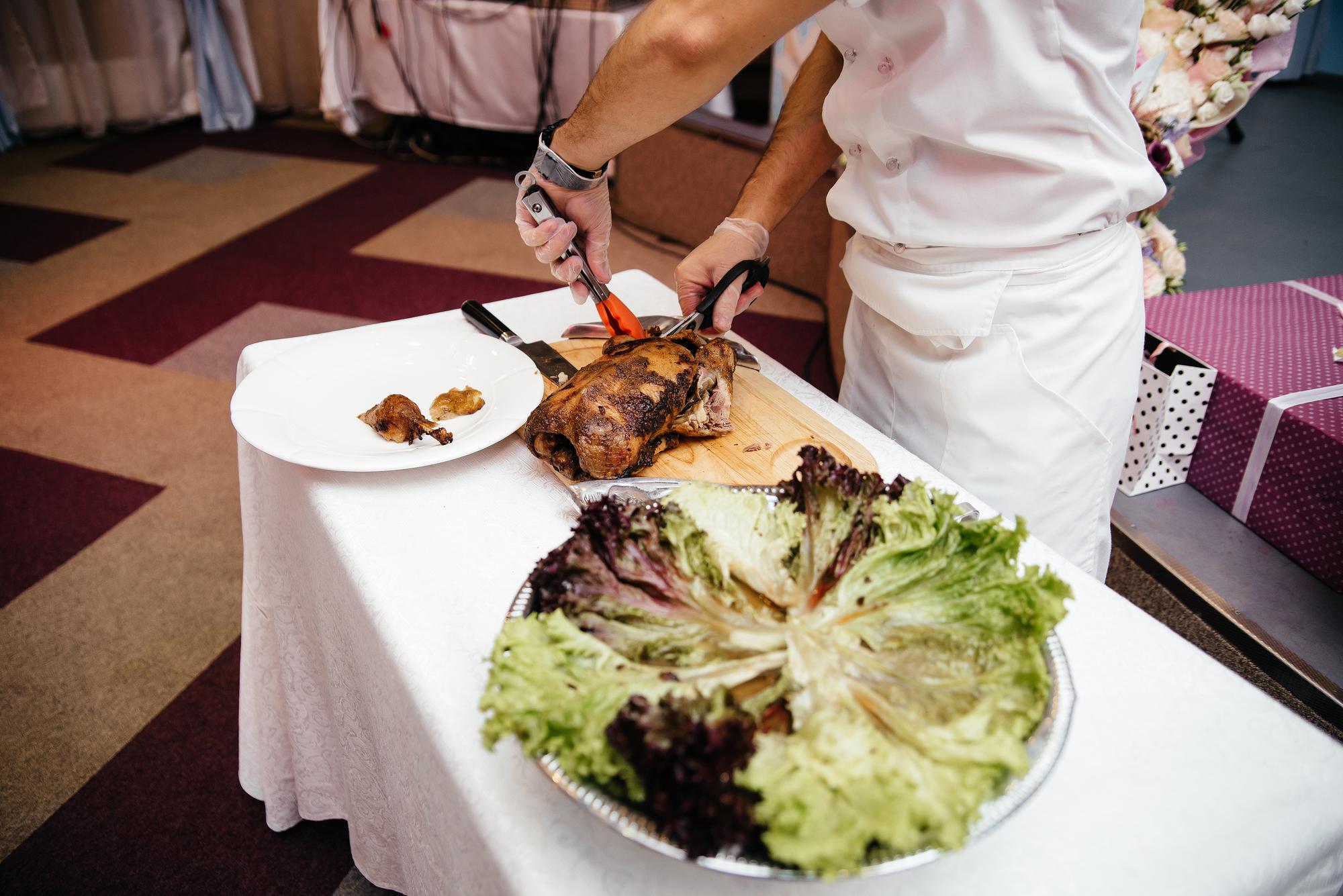Mãos masculinas cortam a carcaça de um grande peru em uma tábua de madeira Carne fresca O cara corta um pássaro em um avental com uma faca