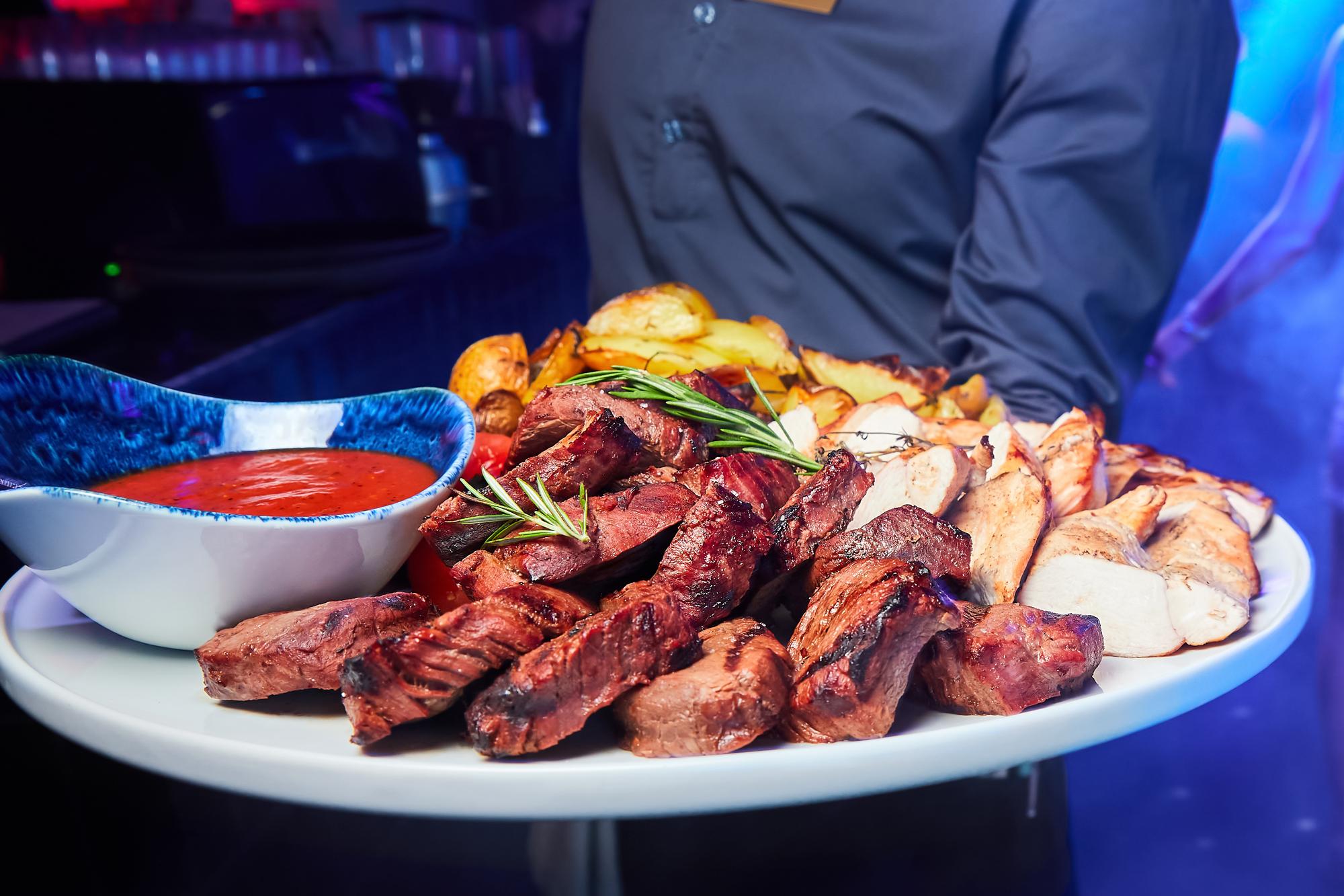 O garçom segura um prato com kebab de carne de porco e frango com batatas assadas, tomate e molho