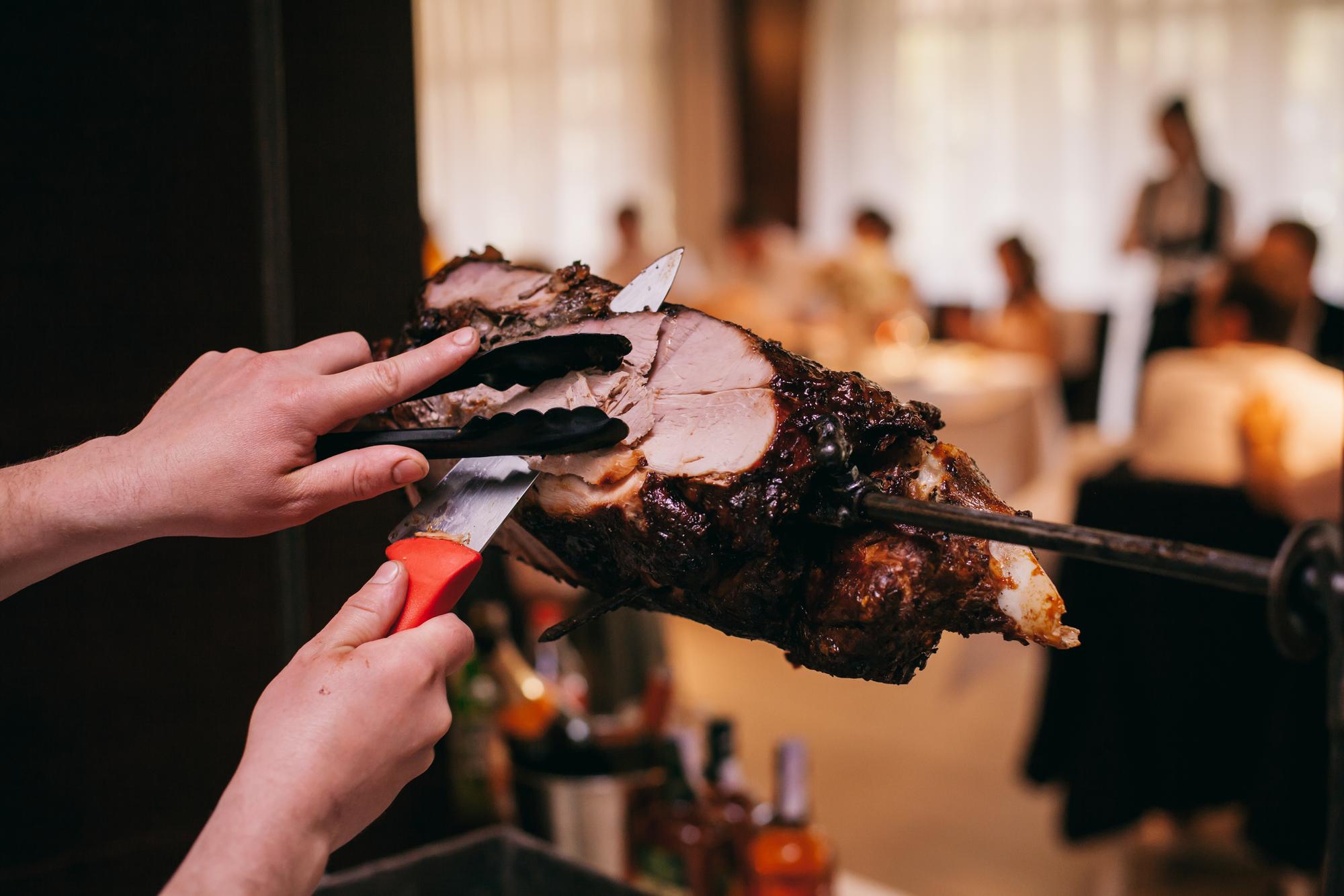 O chef corta a vitela no espeto. vitela no espeto, o chef corta pedaços de carne com uma faca.