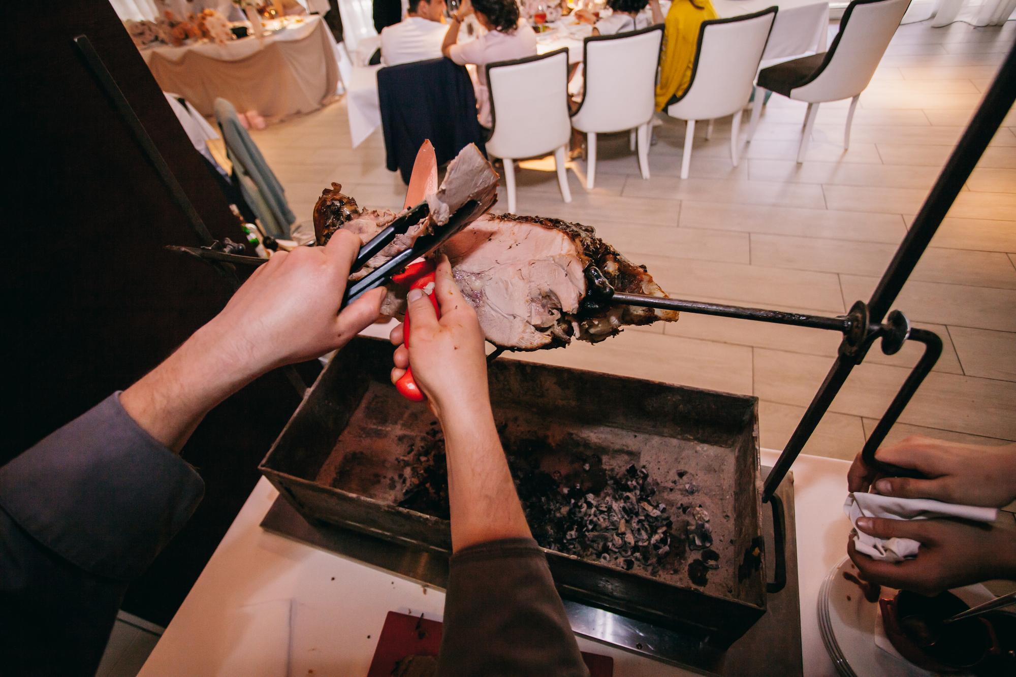 O chef corta a vitela no espeto. vitela no espeto, o chef corta pedaços de carne com uma faca