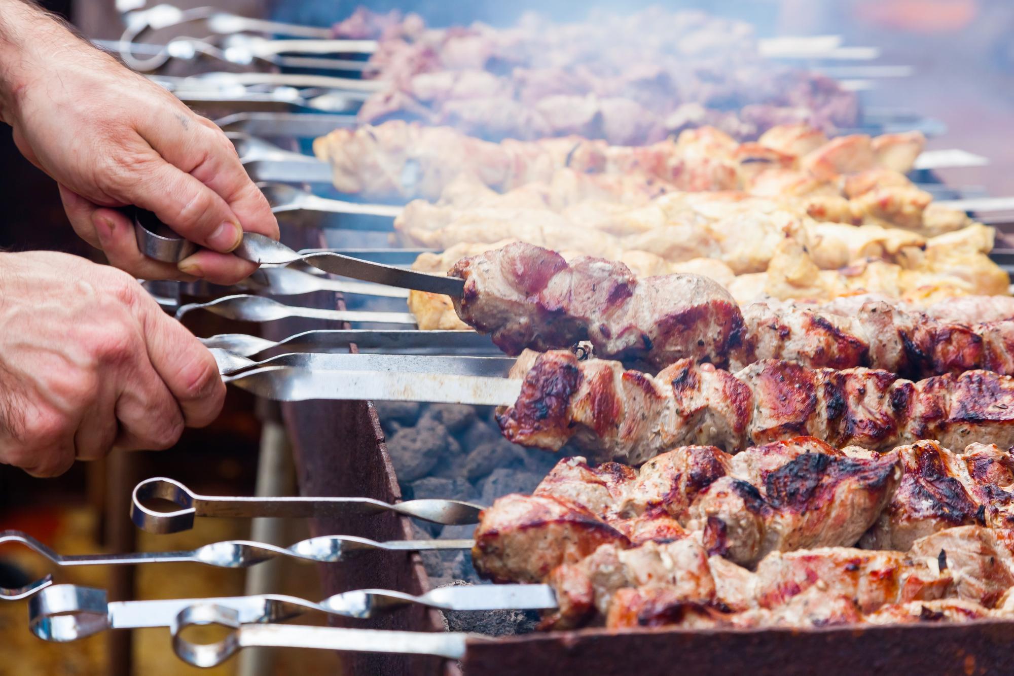 As mãos do homem estão fritando um shish kebab na grelha Frango de porco e carne de cordeiro em espetos na grelha