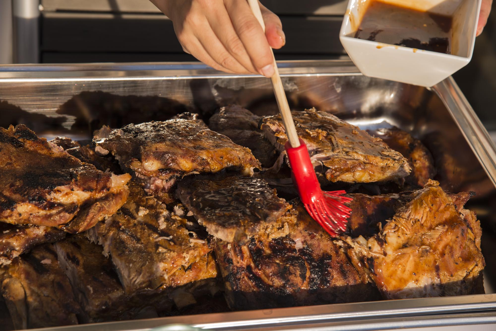 Mão recortada de uma pessoa a cozinhar costelas de churrasco