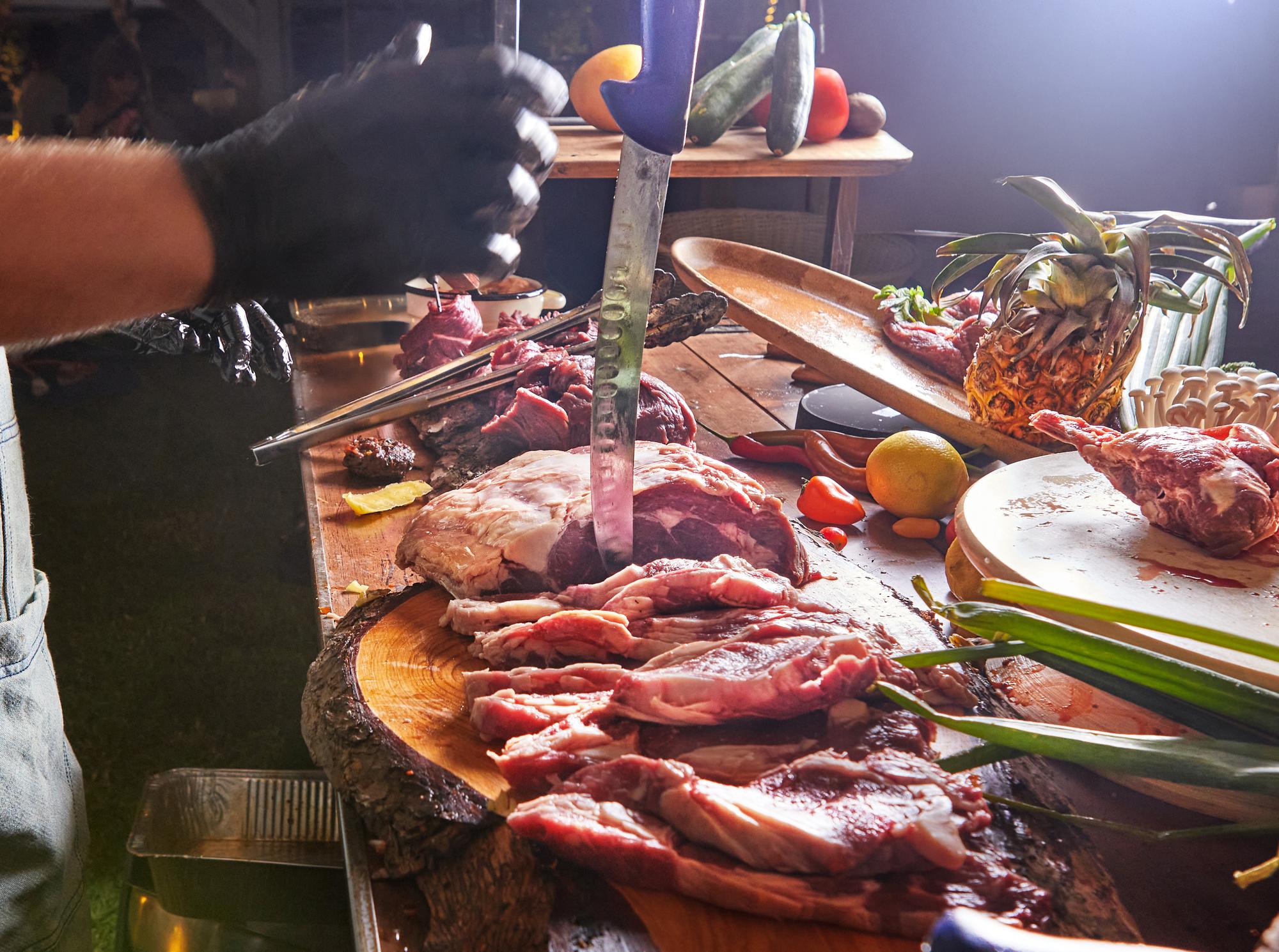 Chef preparando carne crua com faca e luvas
