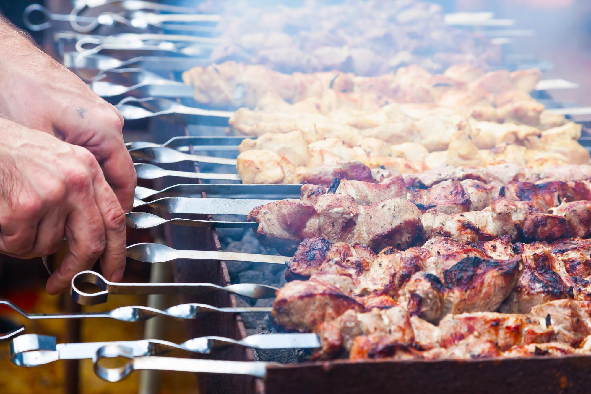 As mãos do homem estão a fritar um shish kebab na grelha, frango de porco e carne de cordeiro em espetos na grelha.