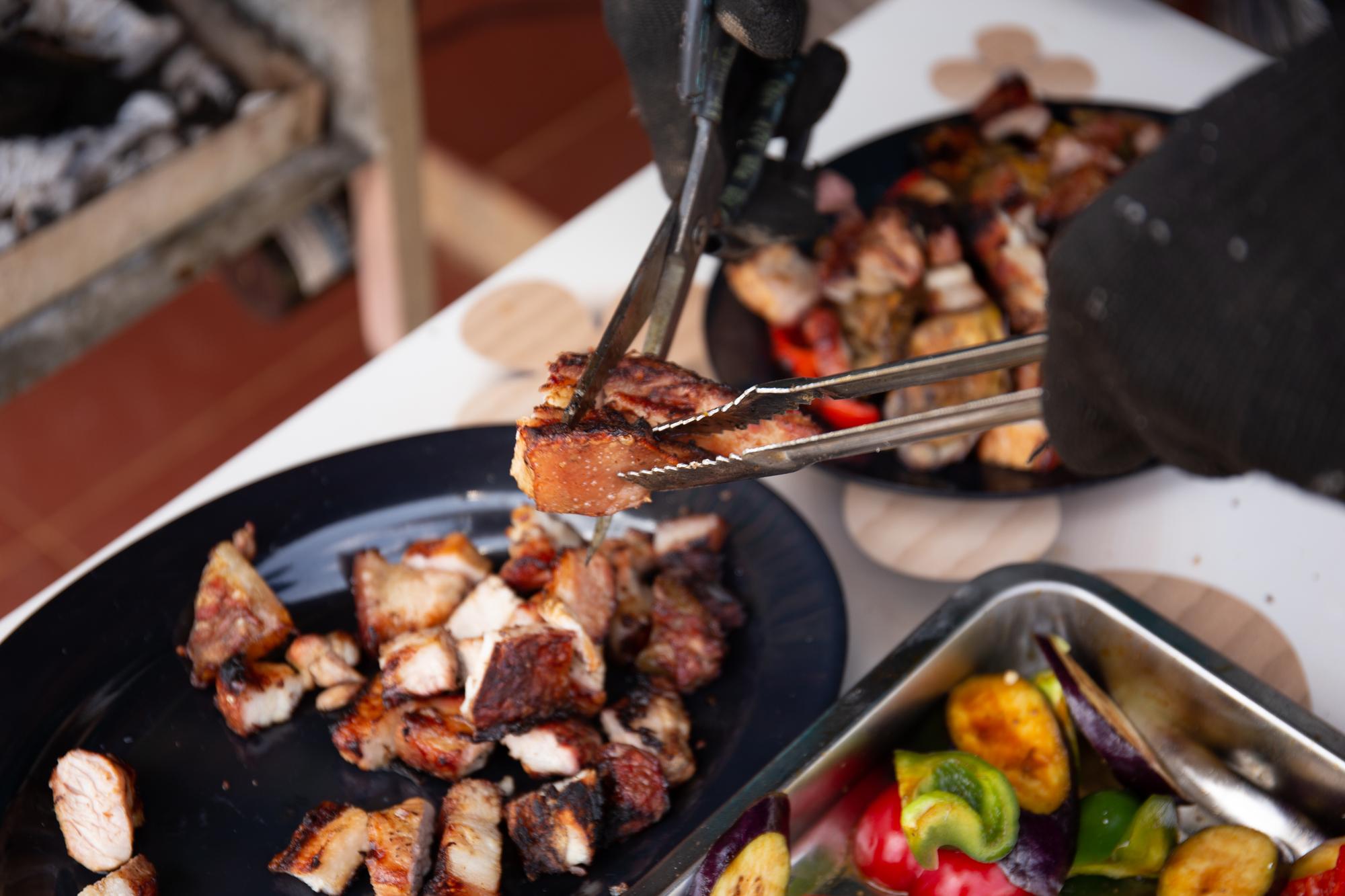 Feche a foto da mão do homem usando uma tesoura para cortar a carne de porco grelhada no prato