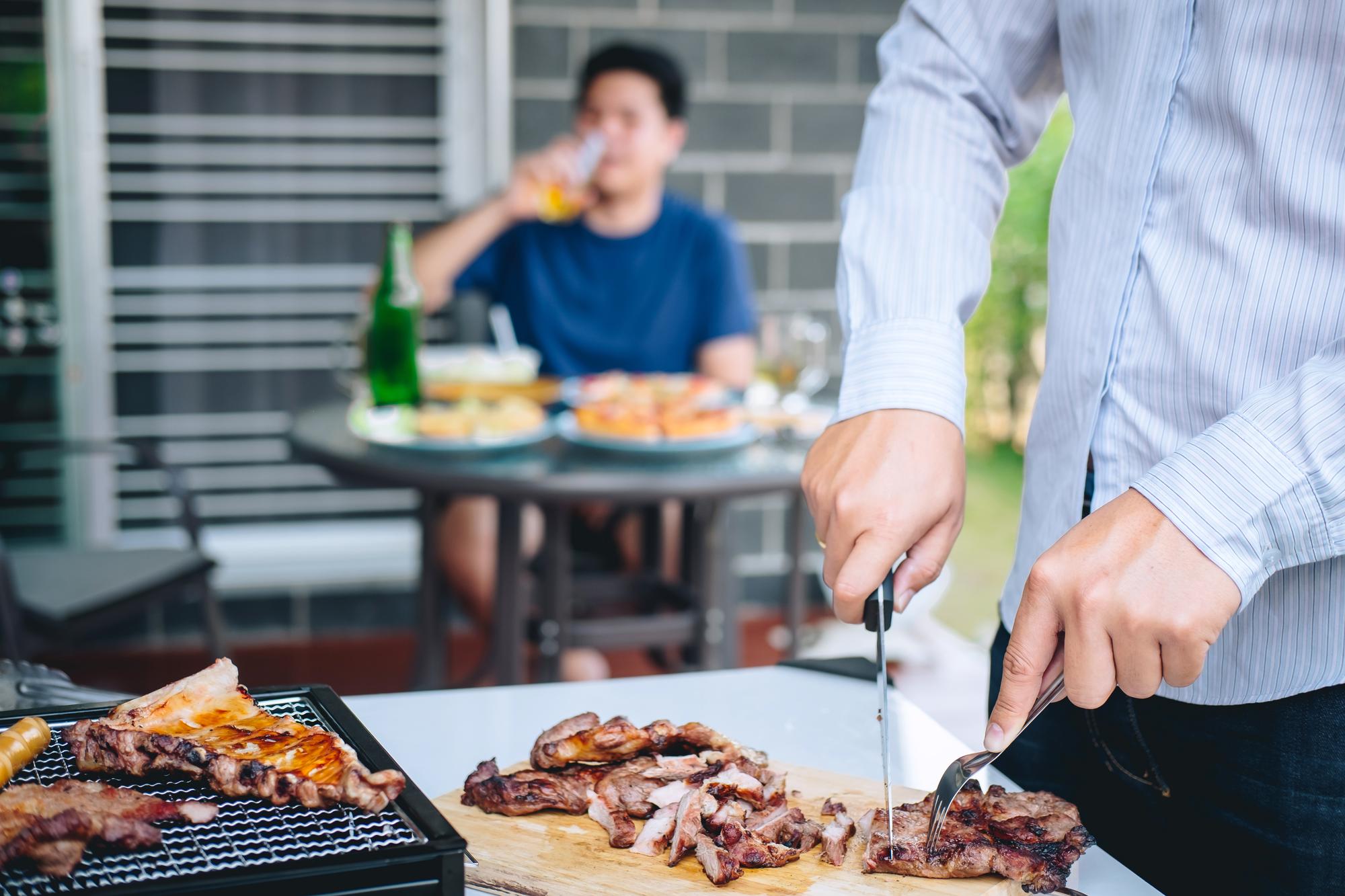 Seção média de um homem cortando carne na mesa com um amigo sentado no fundo