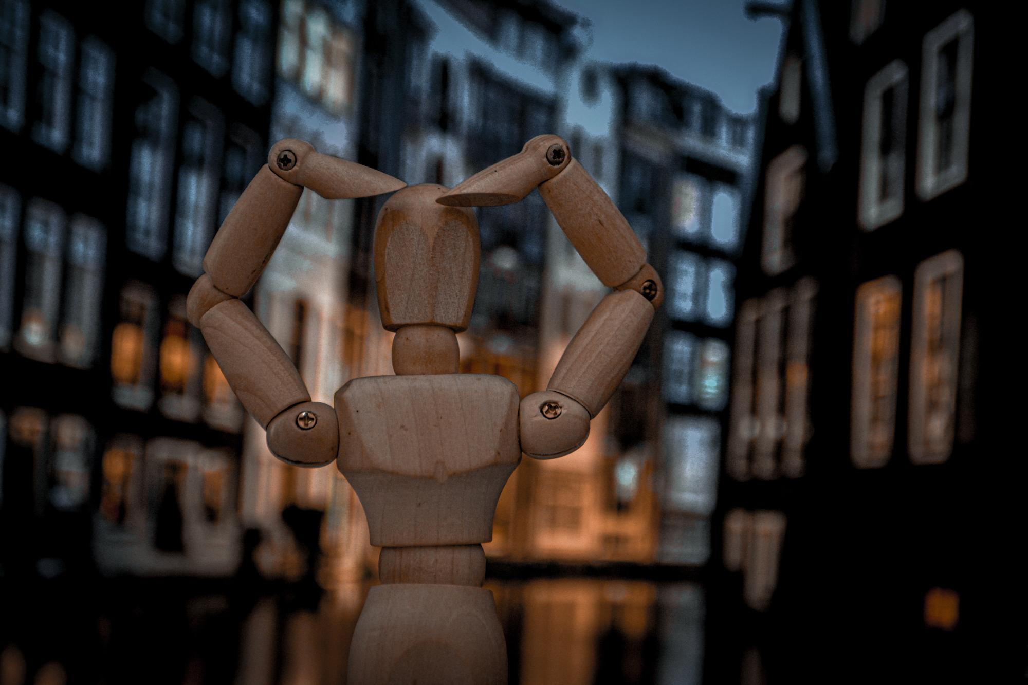 Uma figura de madeira fazendo um gesto de coração com as mãos com a cidade como fundo