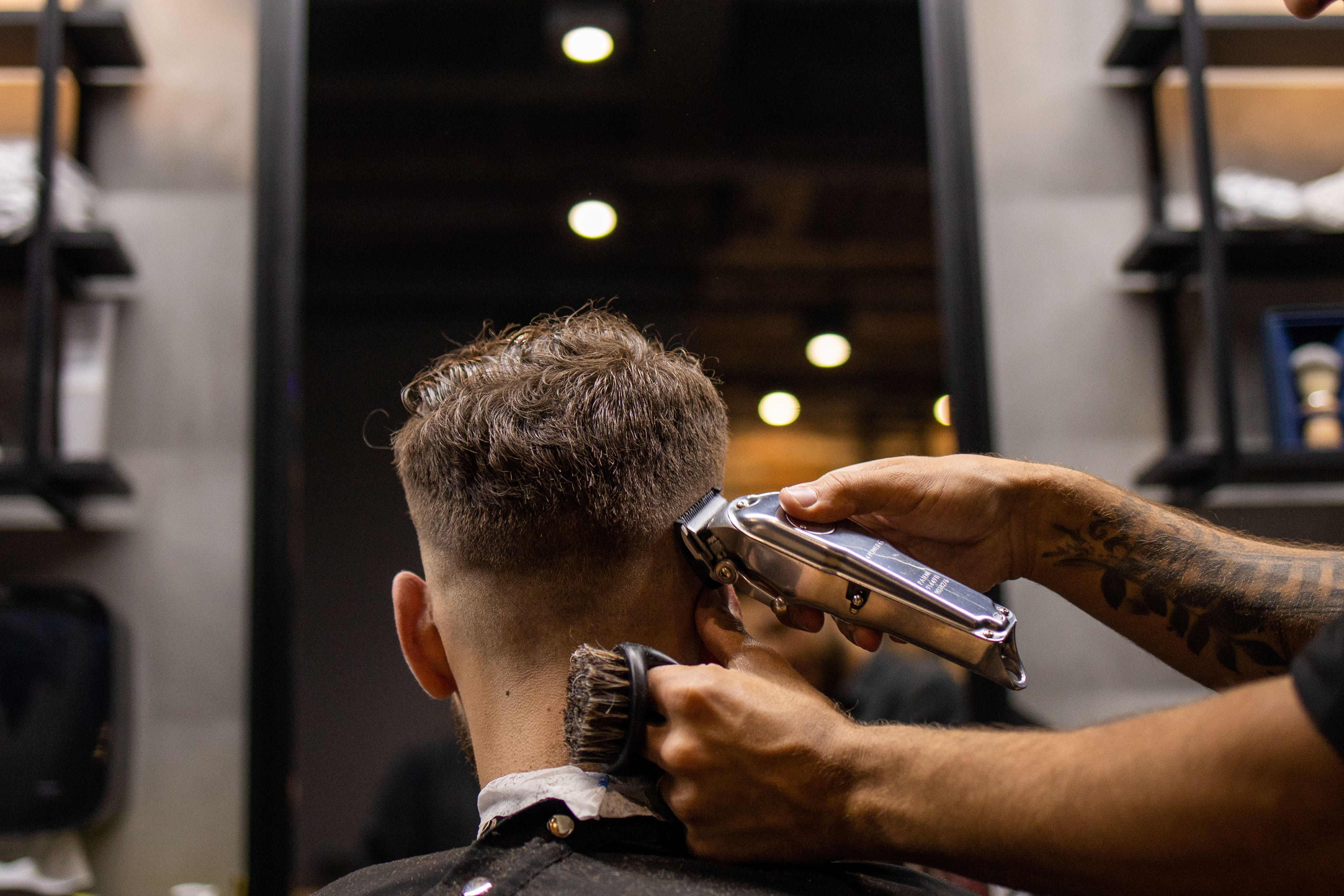 Detalhe de produtos Keune 1922 sendo aplicados em ambiente de barbearia sofisticada com tons de roxo e madeira