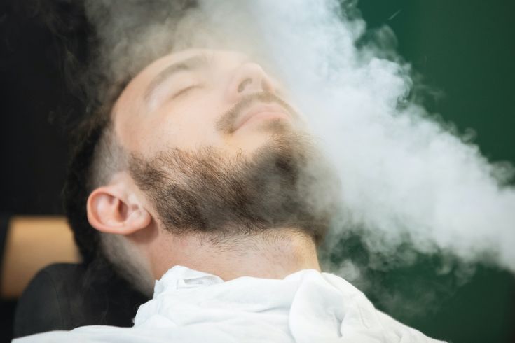 Profissional realizando barboterapia com toalha quente em cliente relaxado em cadeira de massagem