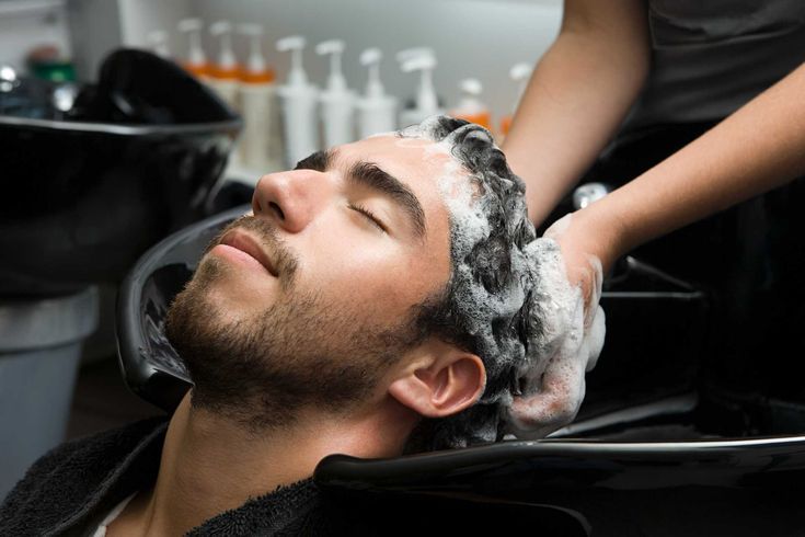 Detalhe de mãos aplicando produto Keune 1922 em cabelo masculino bem cuidado em ambiente de barbearia luxuosa