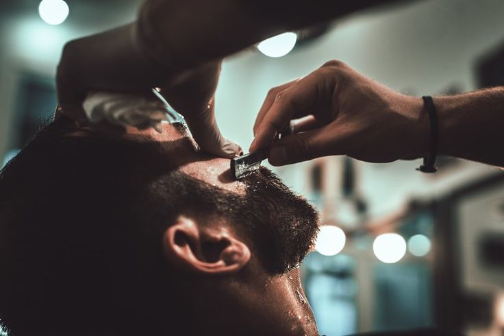 Detalhe de mãos profissionais cuidando da barba de um homem com produtos premium em um ambiente de luz suave e sofisticação