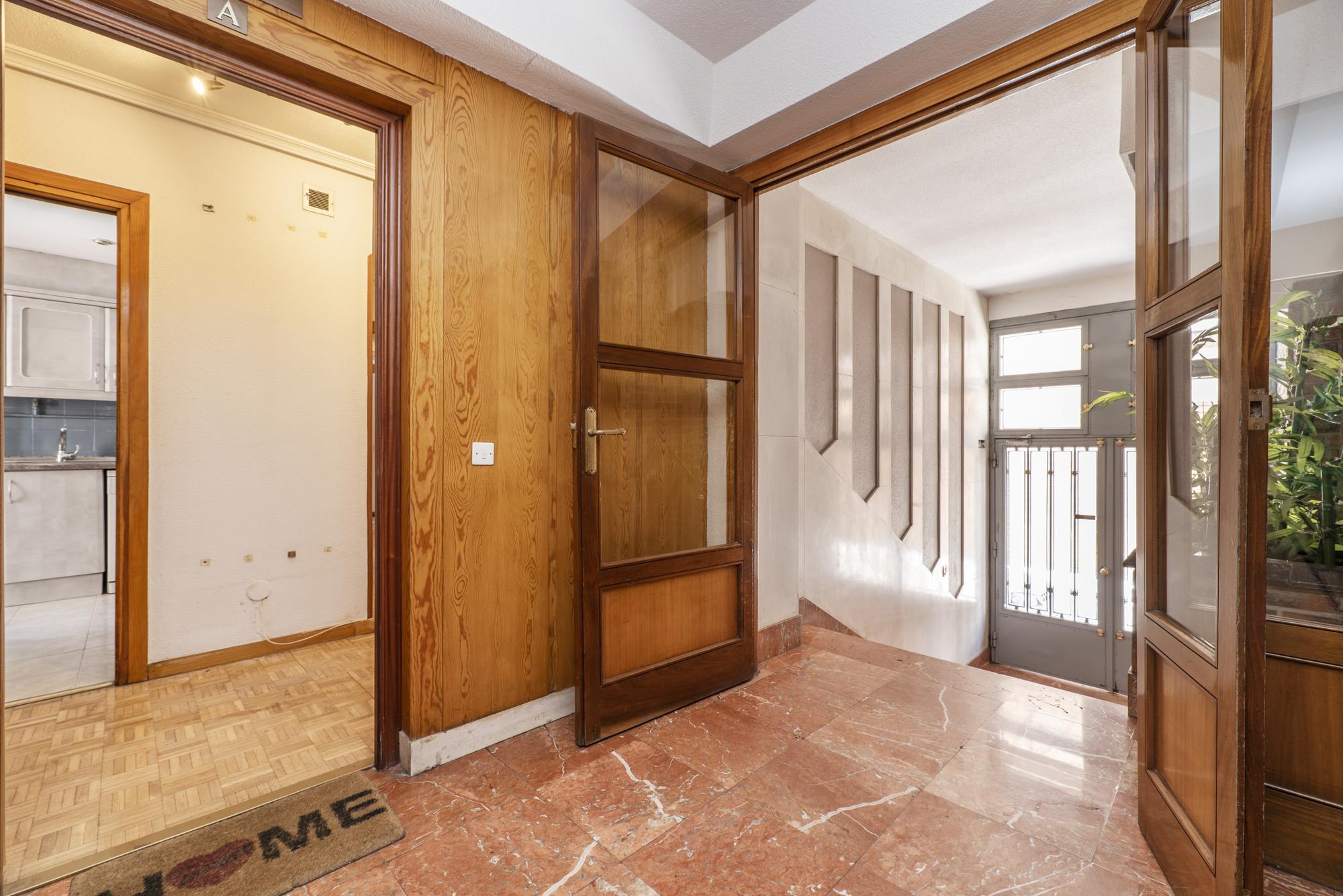 Interior de um portal de uma casa com piso de mármore vermelho tijolo aparente nas paredes e portas de madeira com vidro e acesso a uma casa no mezanino