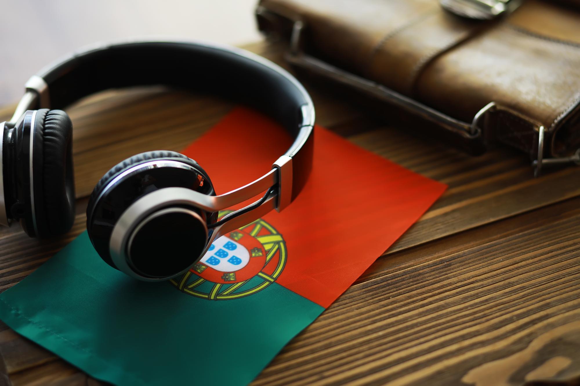 Fones de Ouvido em Mesa de Madeira com Bandeira de Portugal e Agenda de Couro ao Fundo