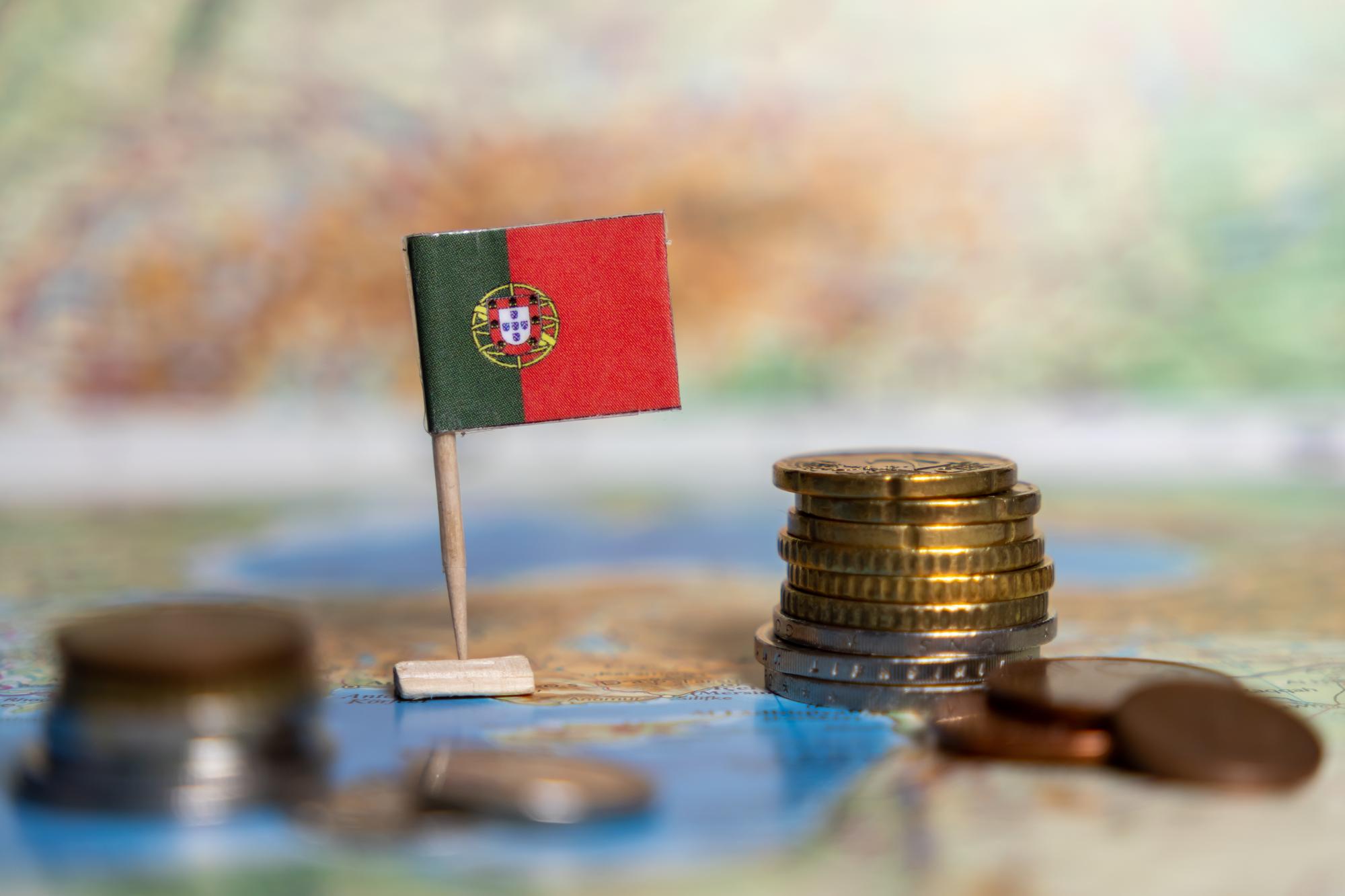 bandeira portuguesa e moedas de euro empilhadas num mapa mundial que representa a economia portuguesa, os sistemas financeiros e as ligações comerciais globais