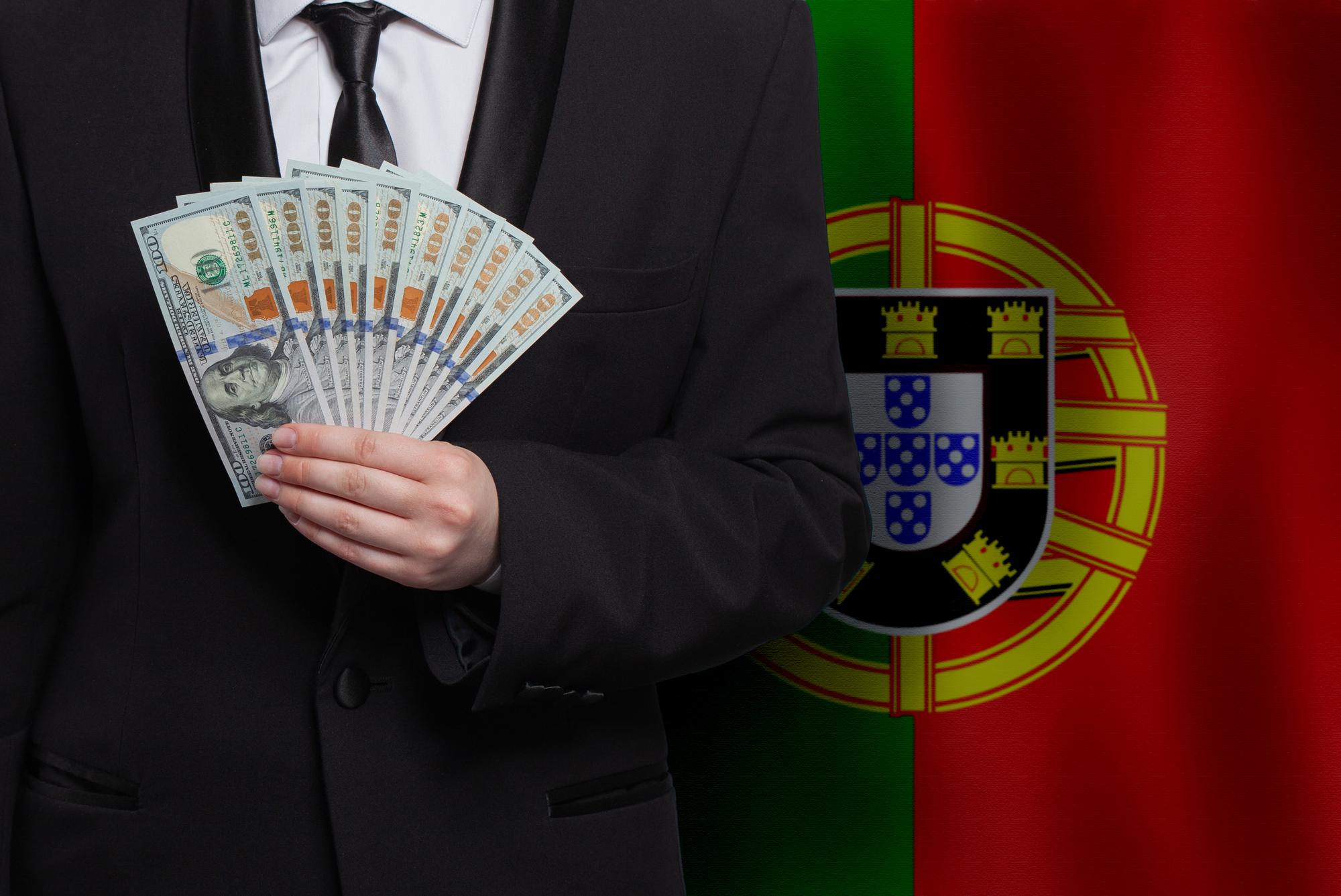 Modelo masculino com notas de dinheiro de 100 dólares contra a bandeira de Portugal