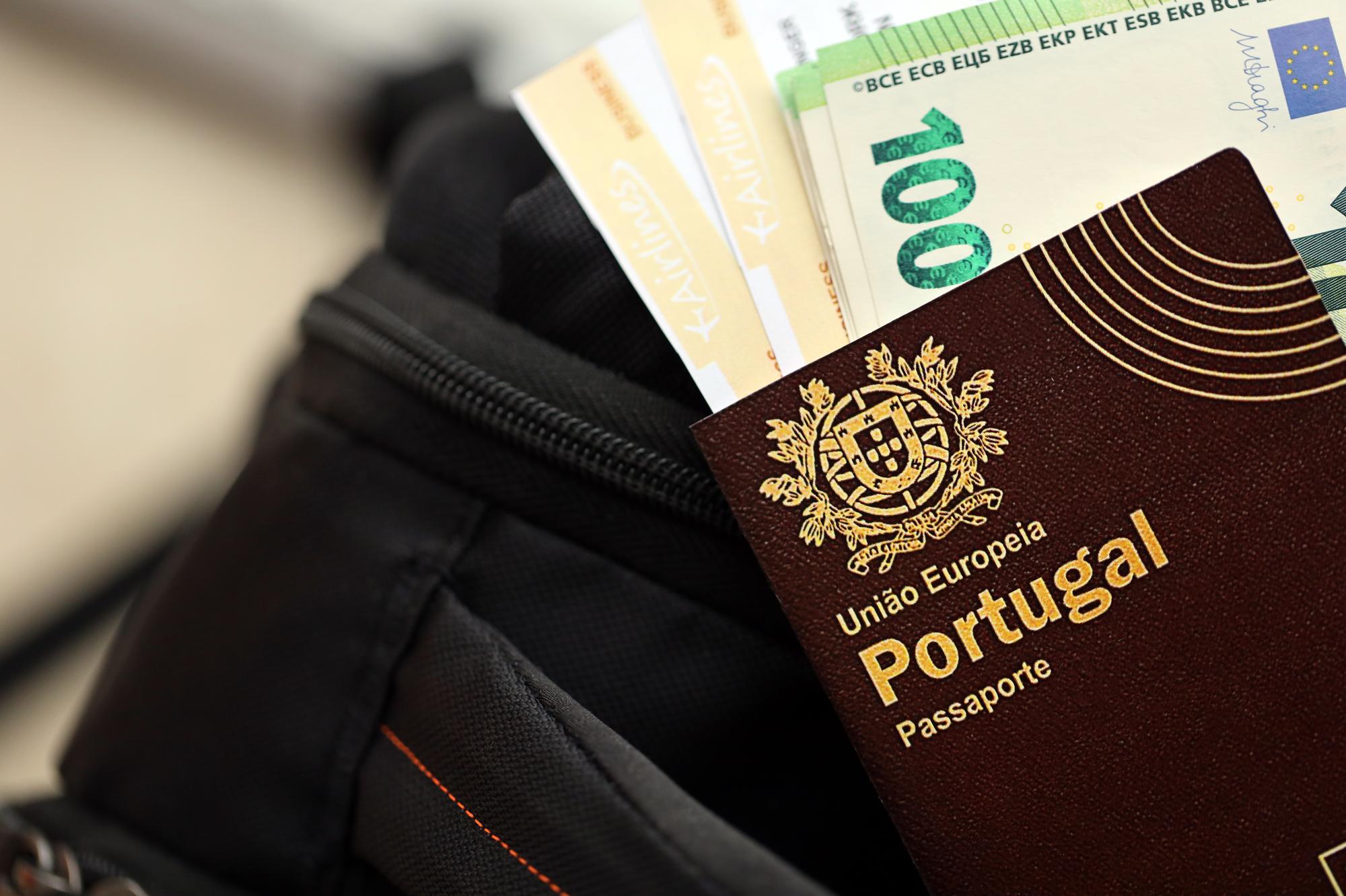 Passaporte português vermelho da União Europeia com dinheiro e bilhetes de avião numa mochila turística