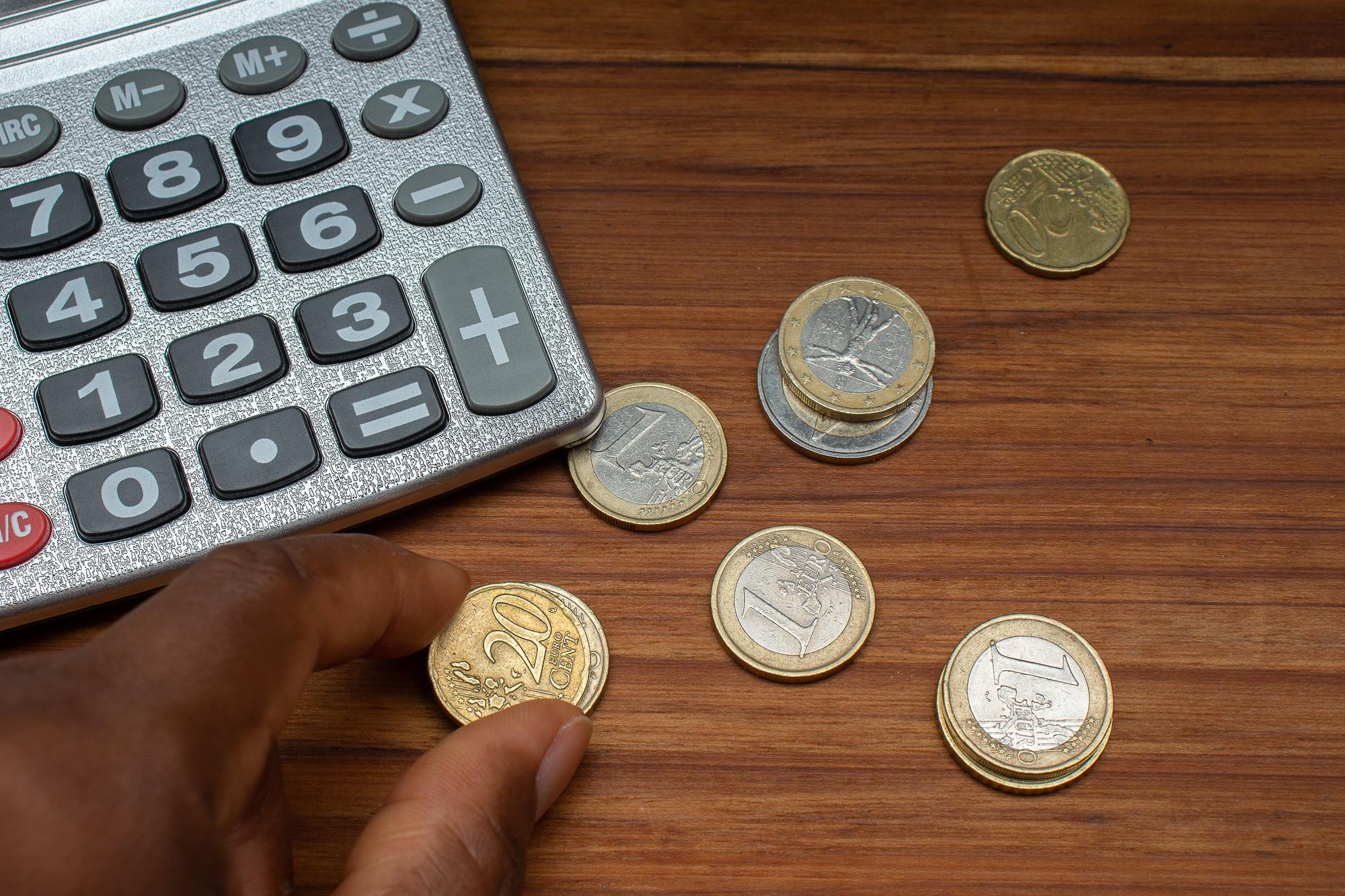XAmão segurando uma moeda perto de uma calculadora