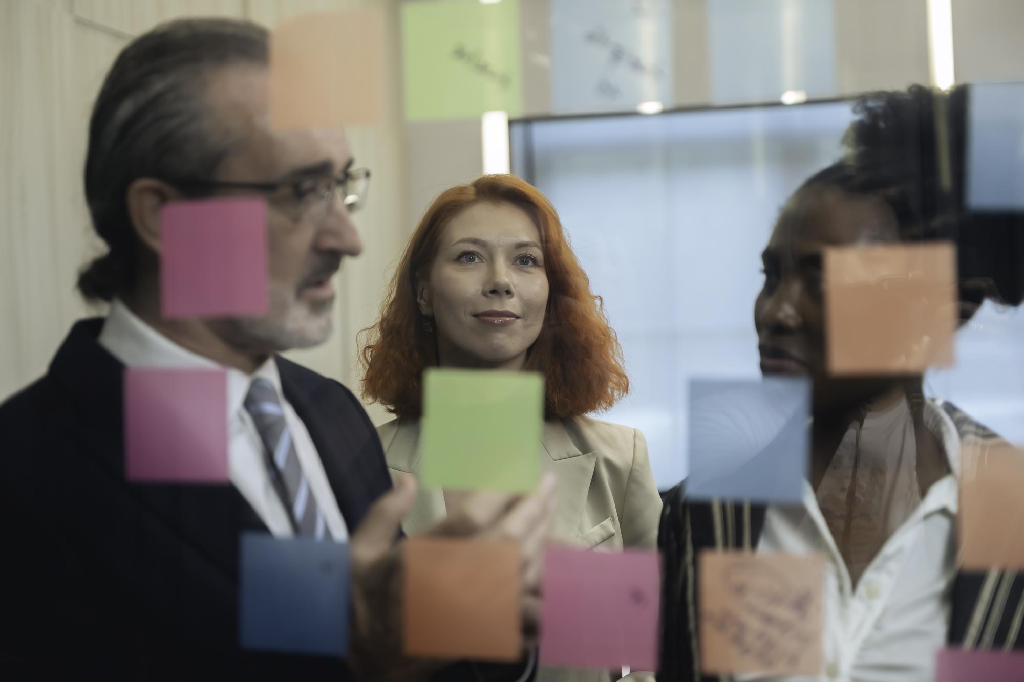 Equipe empresarial diversificada em brainstorming de ideias, usando post-its e tablet digital em um escritório moderno, com foco em trabalho em equipe e colaboração em uma sessão de planejamento criativo.