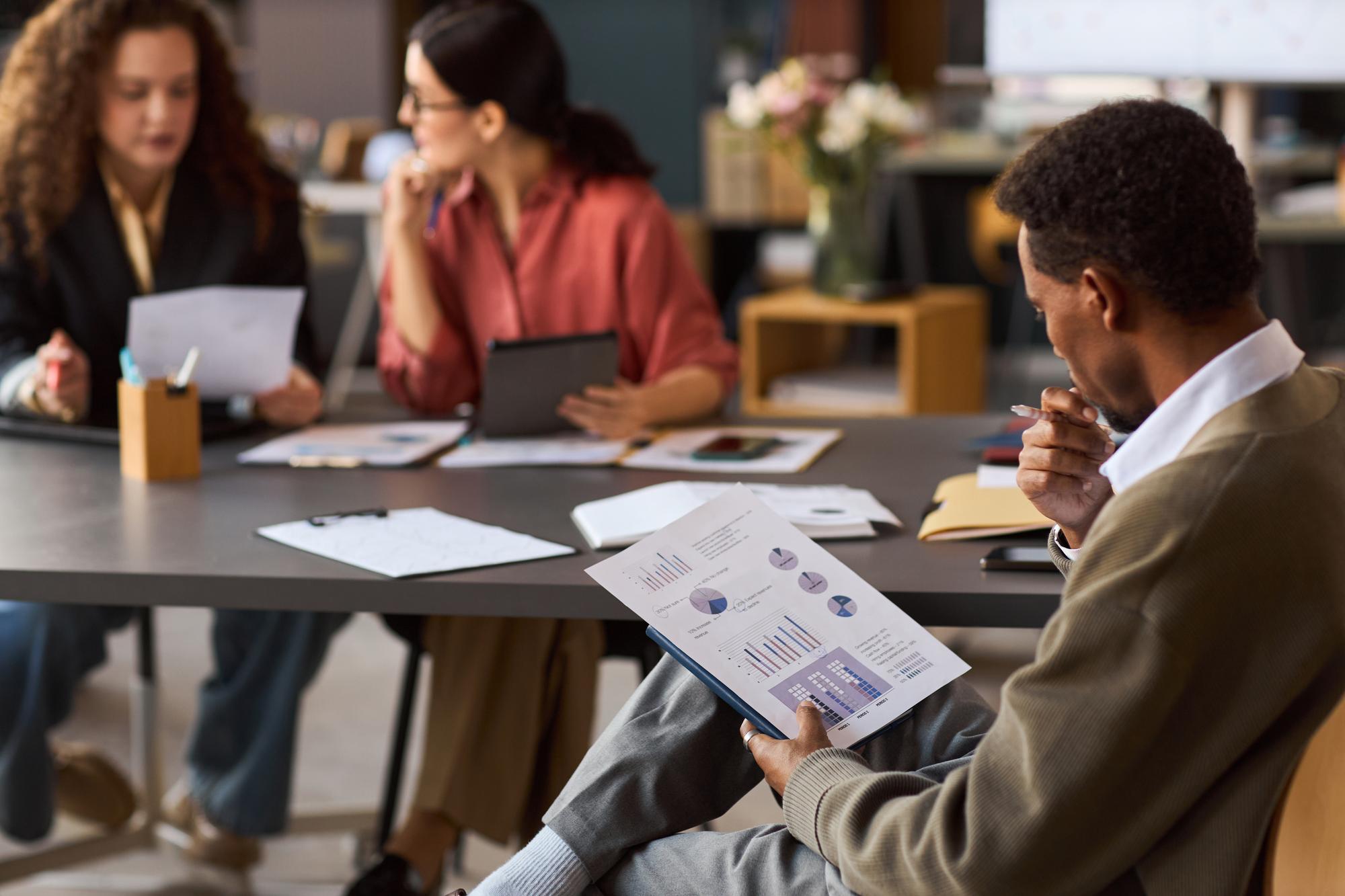 Jovem homem negro analisando gráficos financeiros durante reunião de negócios em ambiente interno