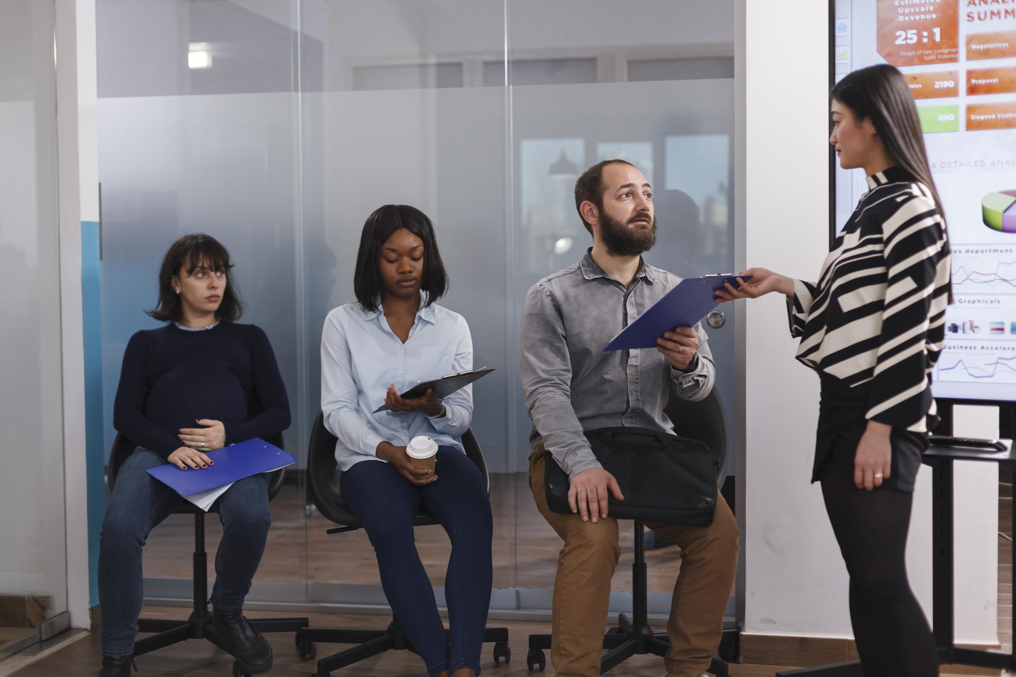 Linda empresária dando prancheta de documentos para homem desempregado esperando na área do lobby da empresa de inicialização. Homem recebendo formulário de emprego do gerente de recrutamento enquanto fala sobre experiência de trabalho.