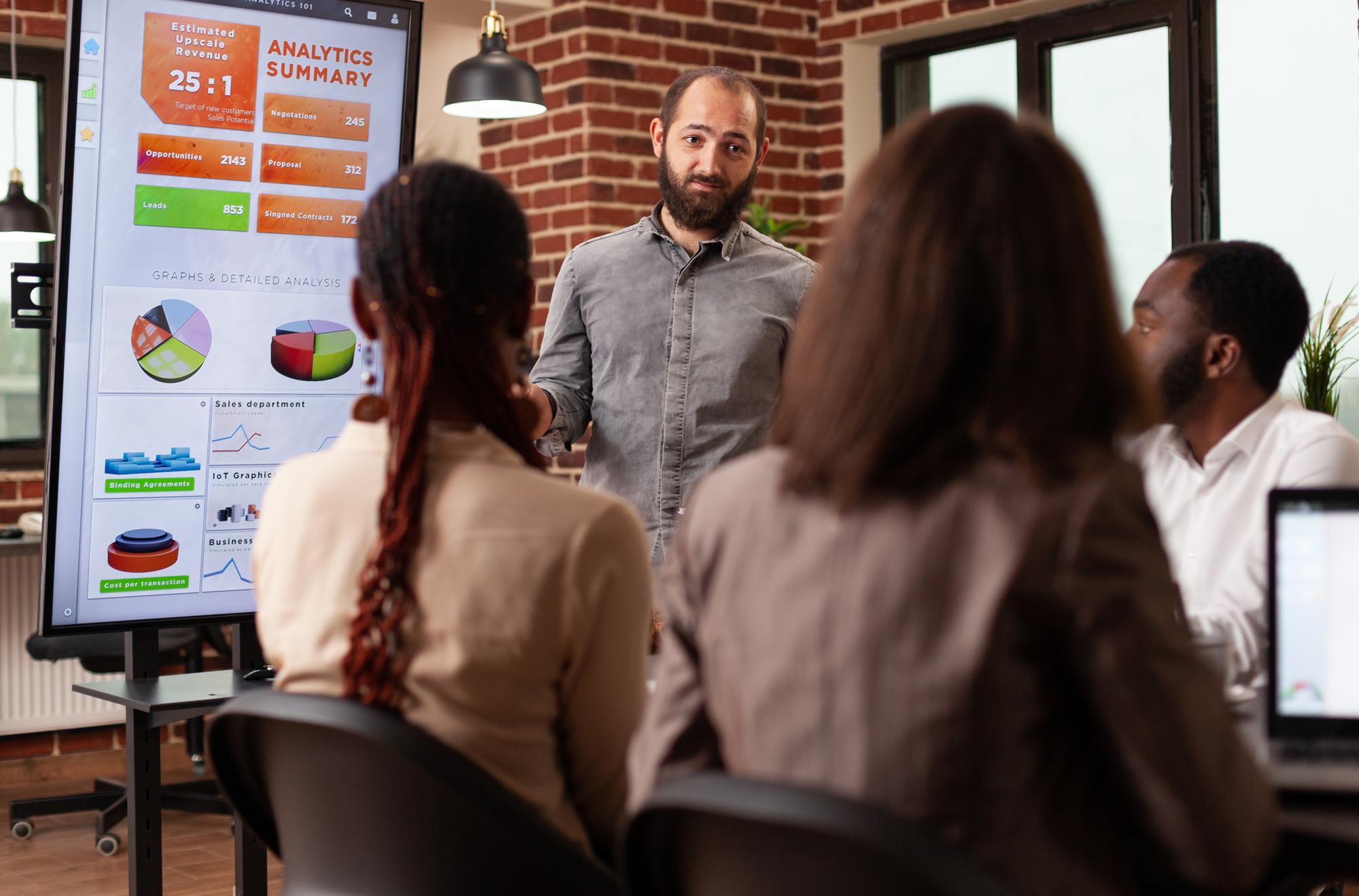 Empresário explicando a apresentação de marketing mostrando a estratégia da empresa usando monitor trabalhando no projeto de negócios no escritório de inicialização. Equipe diversificada sentada na mesa de reunião de ideias de brainstorming