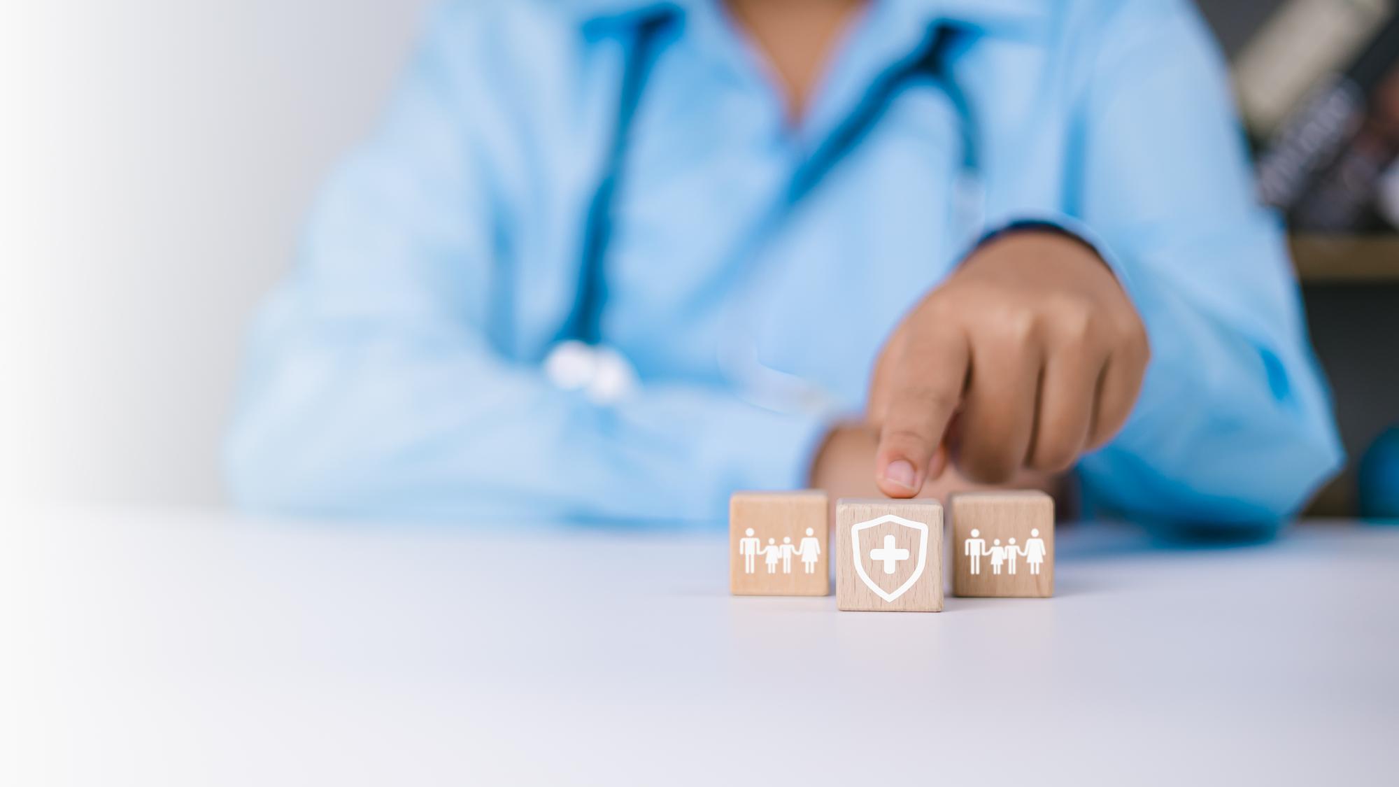 Mãos humanas apontam para proteção seguro de vida e investimento para reduzir o risco O médico seleciona um bloco de madeira com um símbolo de proteção e proteção Planejamento de cuidados de saúde e conceito de seguro